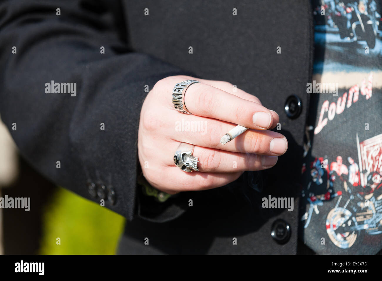Un homme montrant un anneau 'Biker' sur son poing serré tout en tenant une cigarette allumée enroulée entre ses doigts Banque D'Images