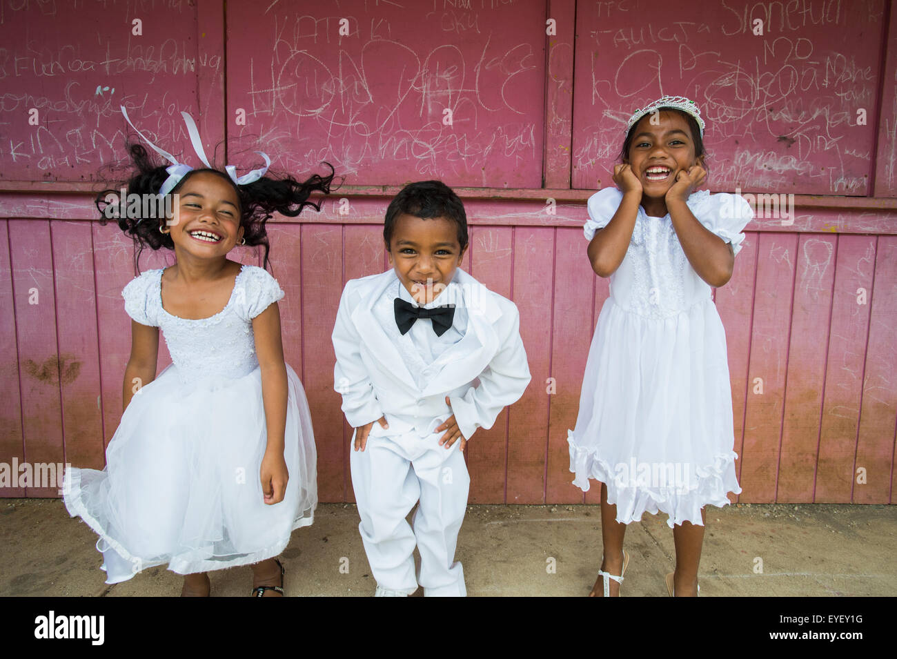 Les enfants vêtus de blanc d'usure formelle contre un mur rouge ; Hapai Island, Tonga Banque D'Images