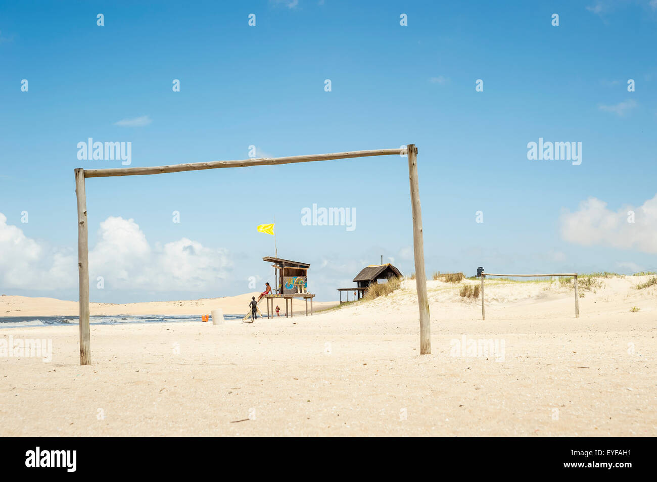 Un poteau en bois sur la plage avec un sauveteur en service dans l'arrière-plan ; Valizas, Uruguay Banque D'Images
