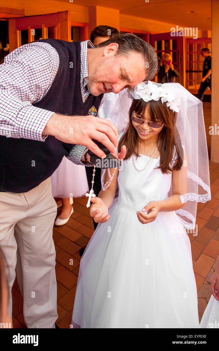 Portant une robe de première communion formelle, une fille lors d'une Laguna Niguel, CA, l'église catholique montre un crucifix sacramentelle à une ministre extraordinaire de la Sainte Eucharistie. Banque D'Images