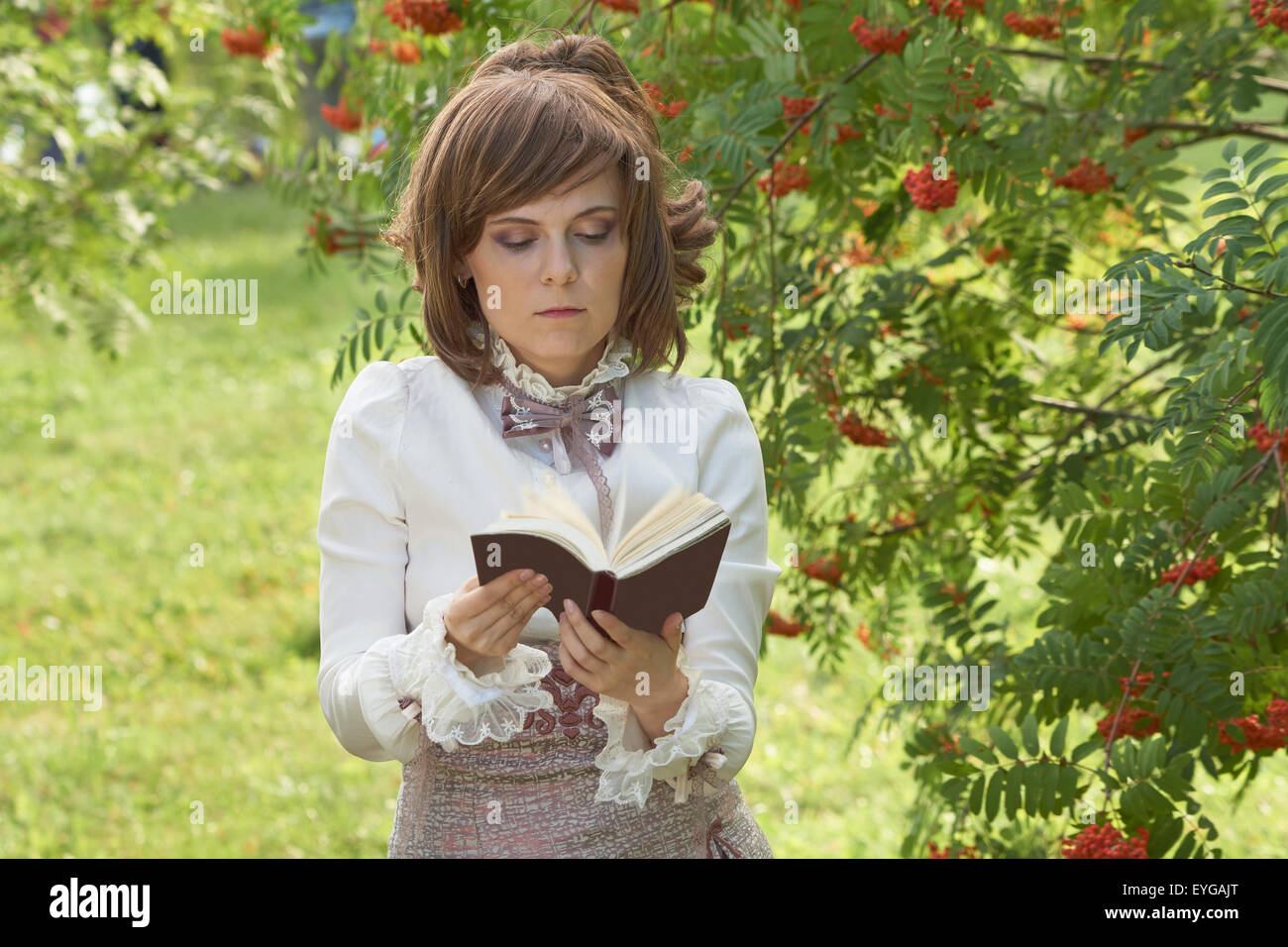 Retro habillé fille feuillette le livre dans le parc d'été Banque D'Images