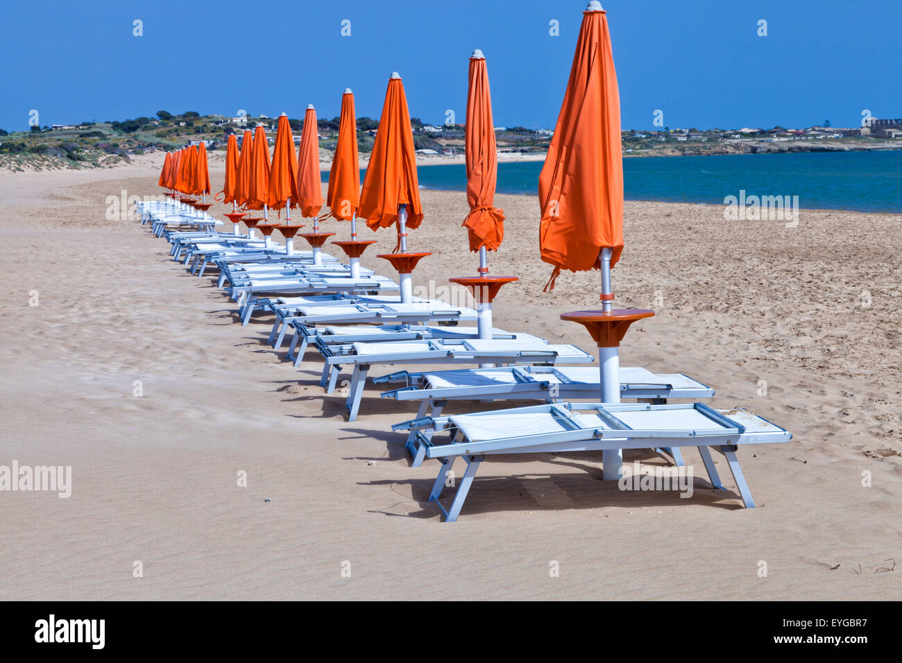 Orange soleil parasols fermés en plastique blanc avec des chaises de détente sur une plage de sable de la Méditerranée, la Sicile, aux beaux jours d'été Banque D'Images