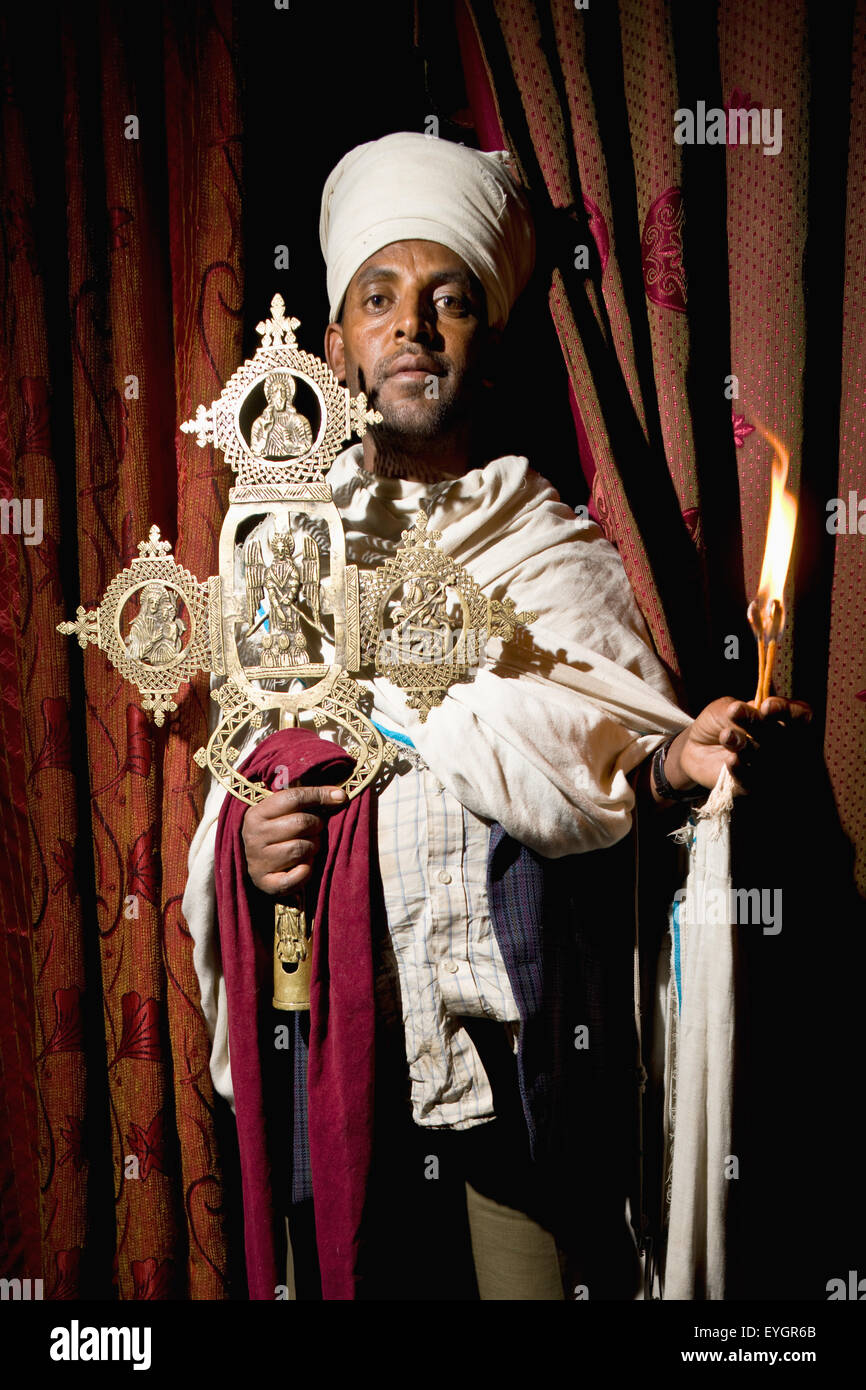 Nord de l'Éthiopie, prêtre orthodoxe éthiopienne traditionnelle holding cross et bougie allumée dans Yemrehanna Krestos Église ; Lalibela Banque D'Images