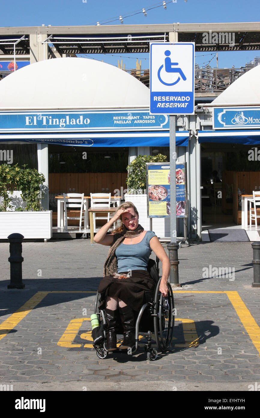 Femme à l'aide d'un fauteuil roulant dans une place de stationnement handicapé Banque D'Images