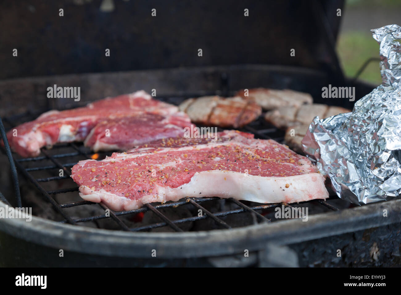 T-bone steaks sit sooking avec d'autres aliments sur un gril de charbon de bois Banque D'Images