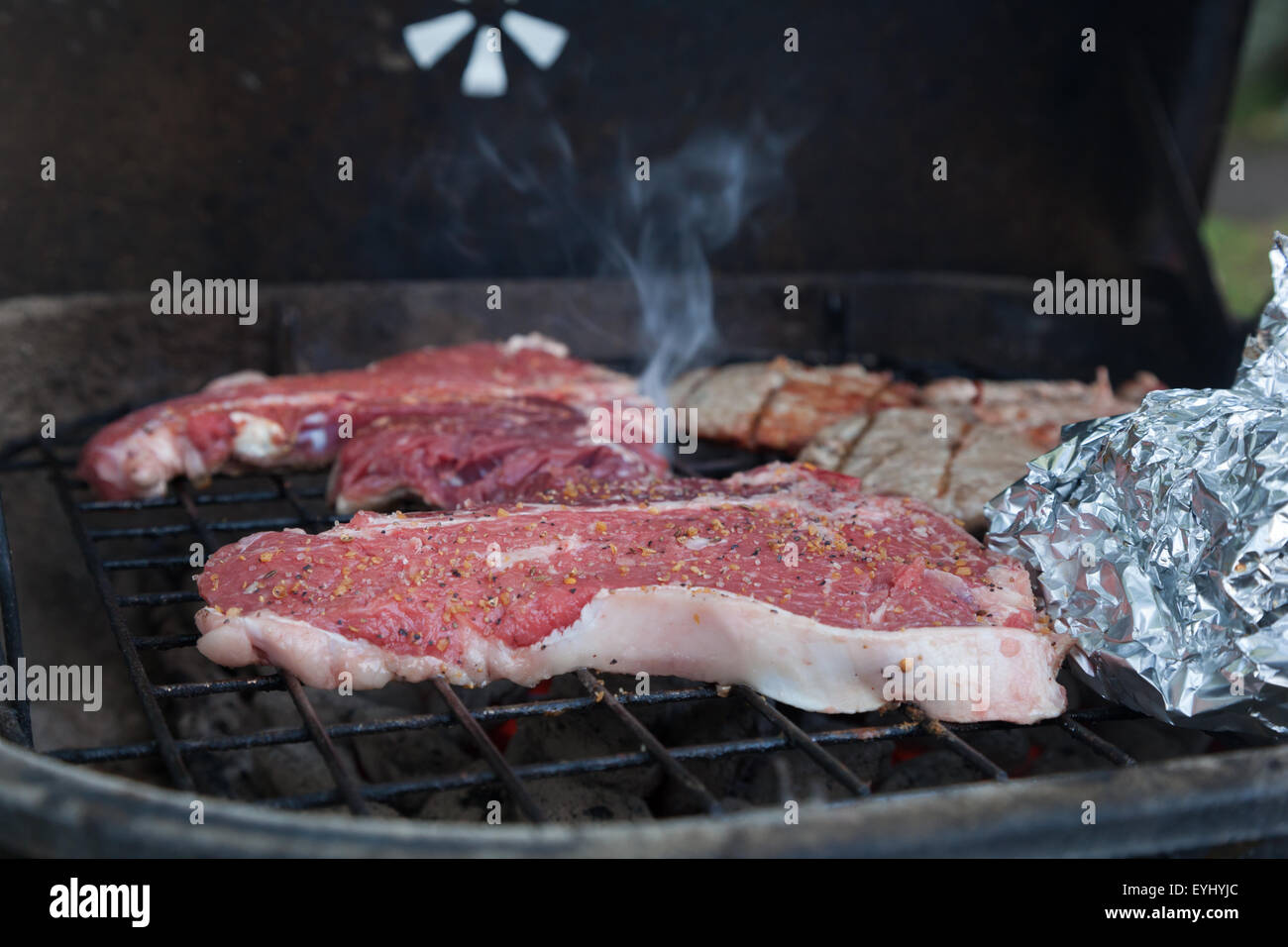 T-bone steaks sit sooking avec d'autres aliments sur un gril de charbon de bois Banque D'Images