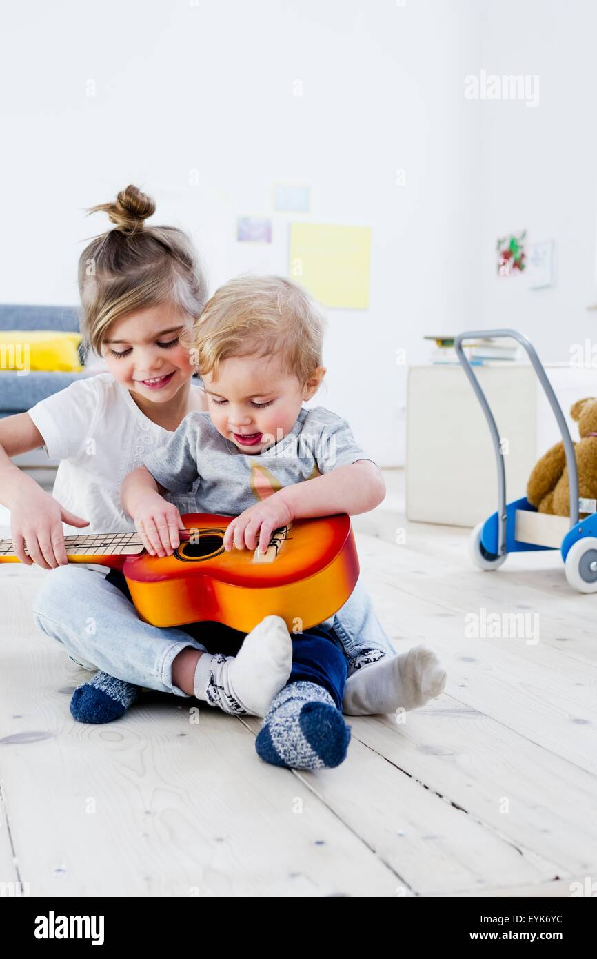 Frère et sœur jouant guitare jouet à la maison Banque D'Images