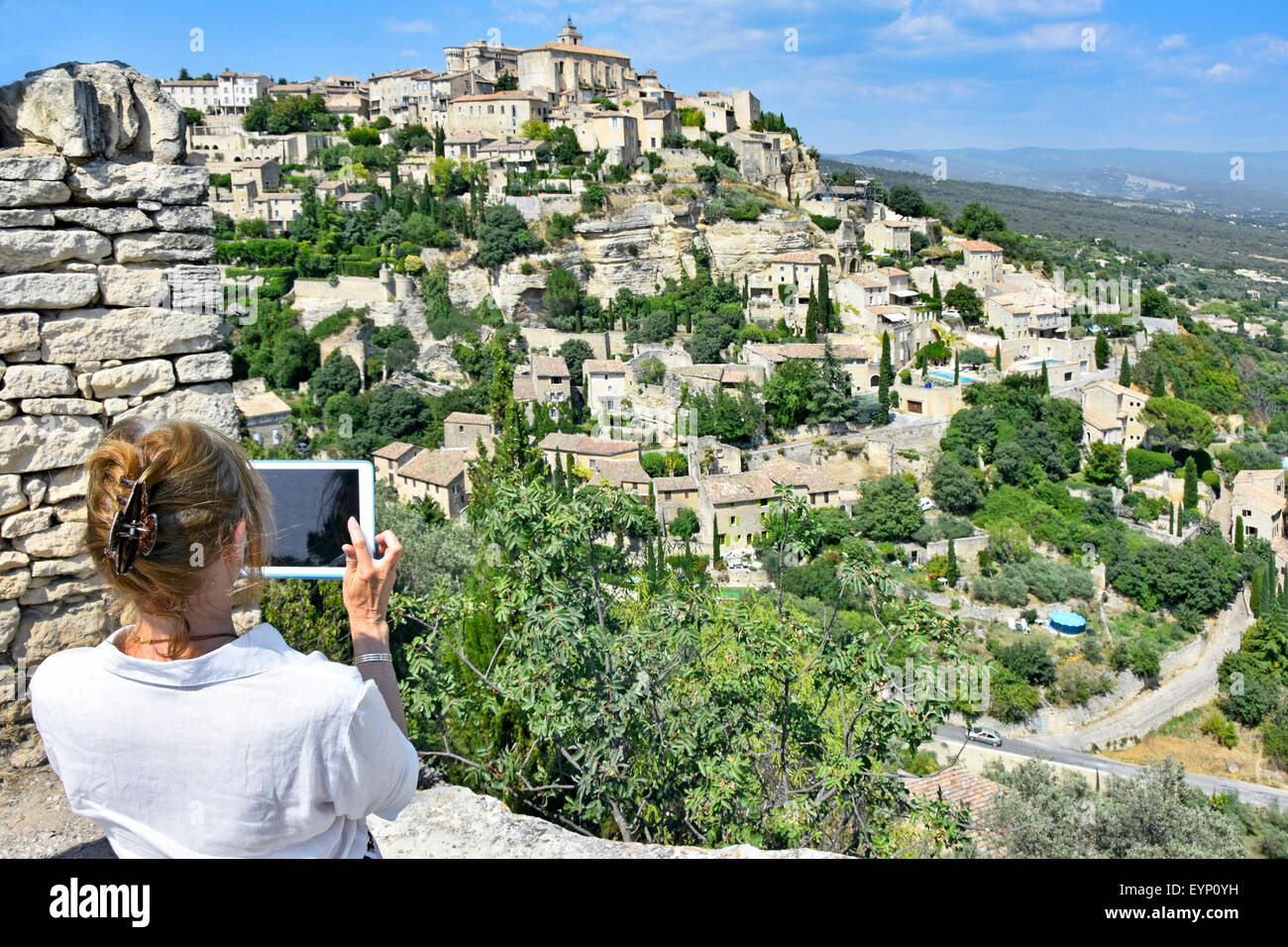 Femme tenant un ipad pour composer et prendre une photo de la colline française pittoresque village de Gordes Provence Sud de la France Banque D'Images