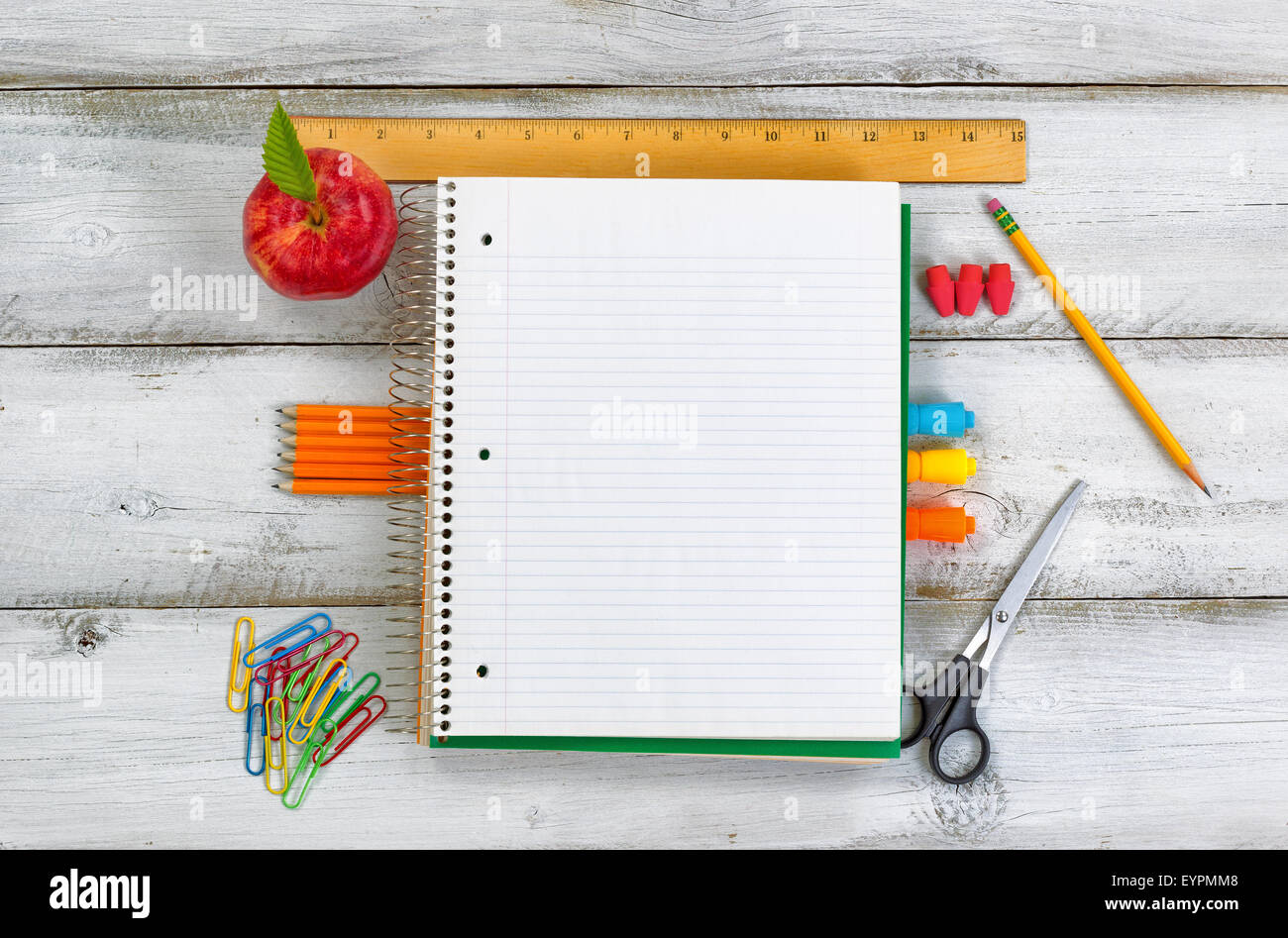 Les fournitures scolaires formant frontière sur le bloc-notes avec bois blanc rustique comme arrière-plan. Banque D'Images