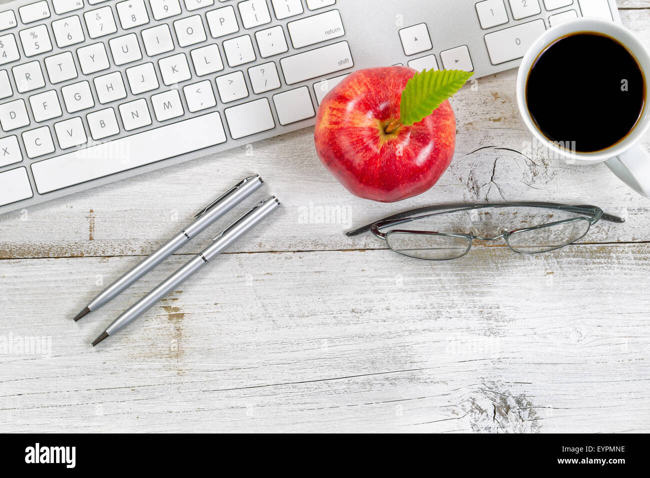 Pomme Rouge, café, lunettes de lecture et d'argent des stylos à côté du clavier de l'ordinateur de bureau blanc rustique en dessous. Banque D'Images