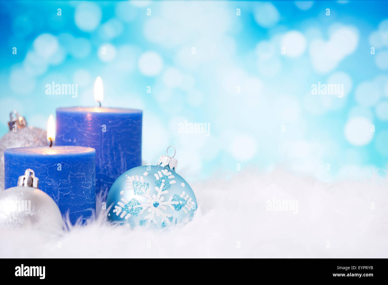 Bleu et argent boules de Noël et des bougies sur une surface à plumes en face de defocused lights bleu et blanc. Banque D'Images