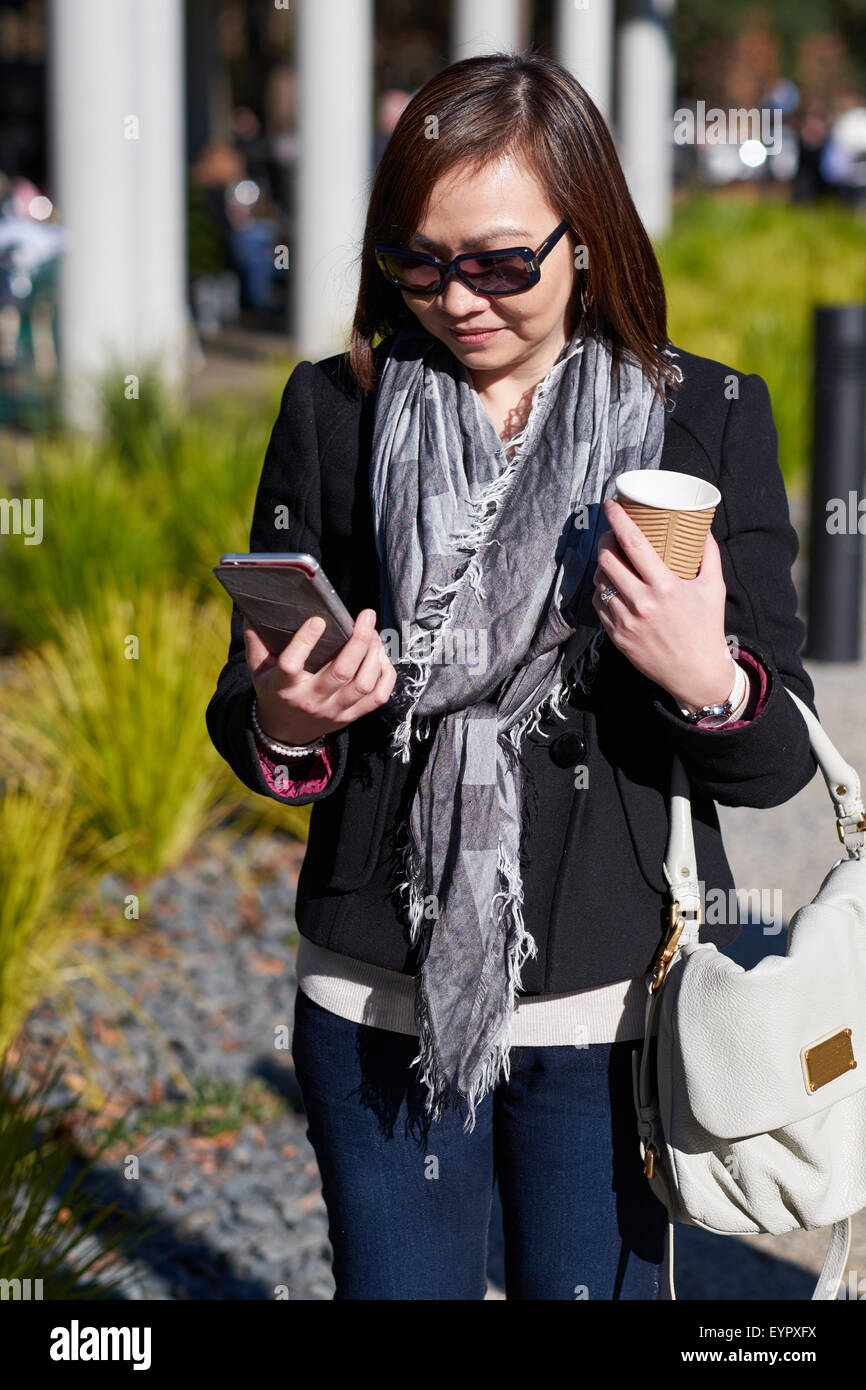 Woman walking looking at phone avec le café dans la main Banque D'Images