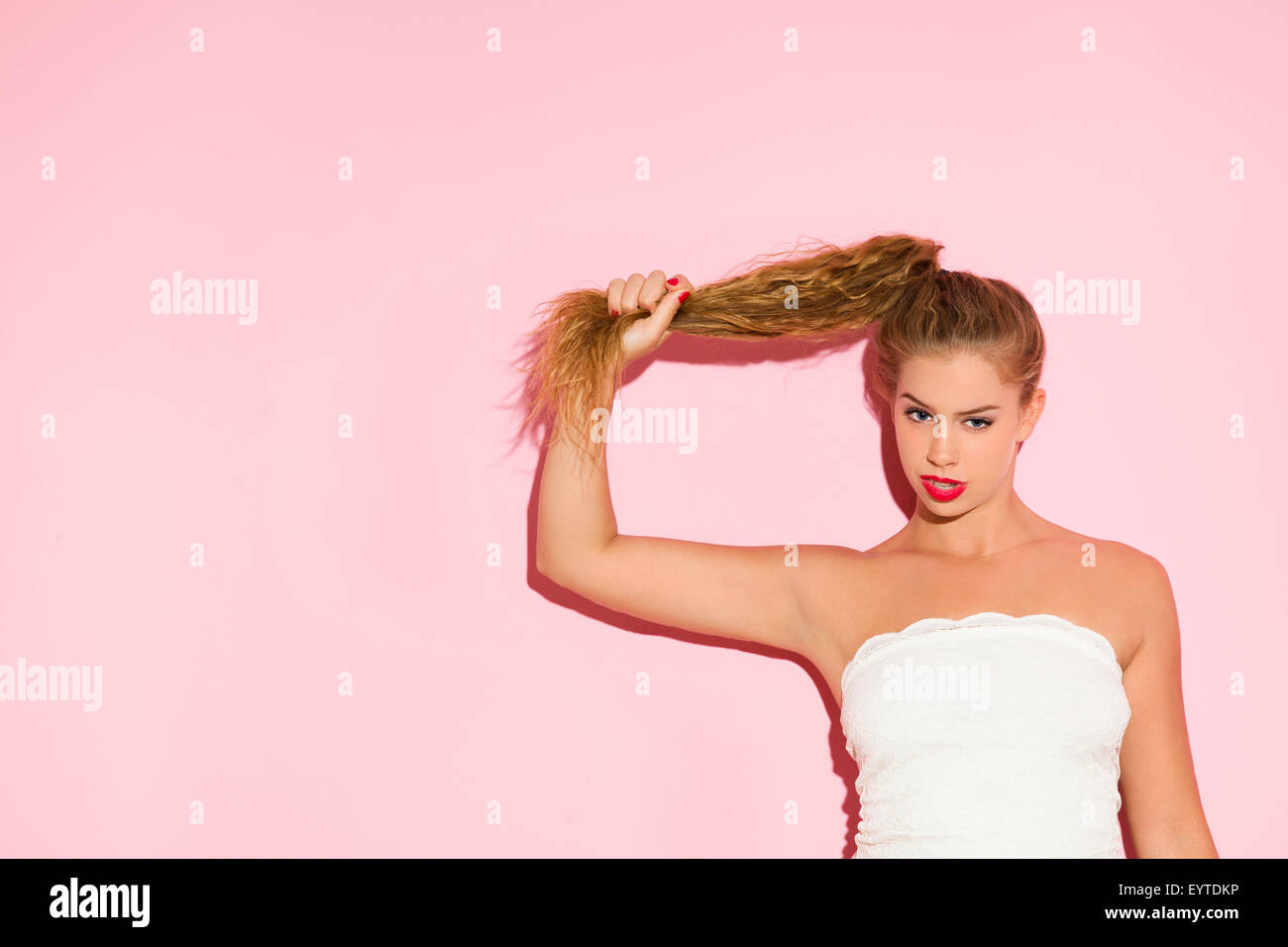 Portrait d'une jeune femme en face de mur rose, tirant les cheveux Banque D'Images
