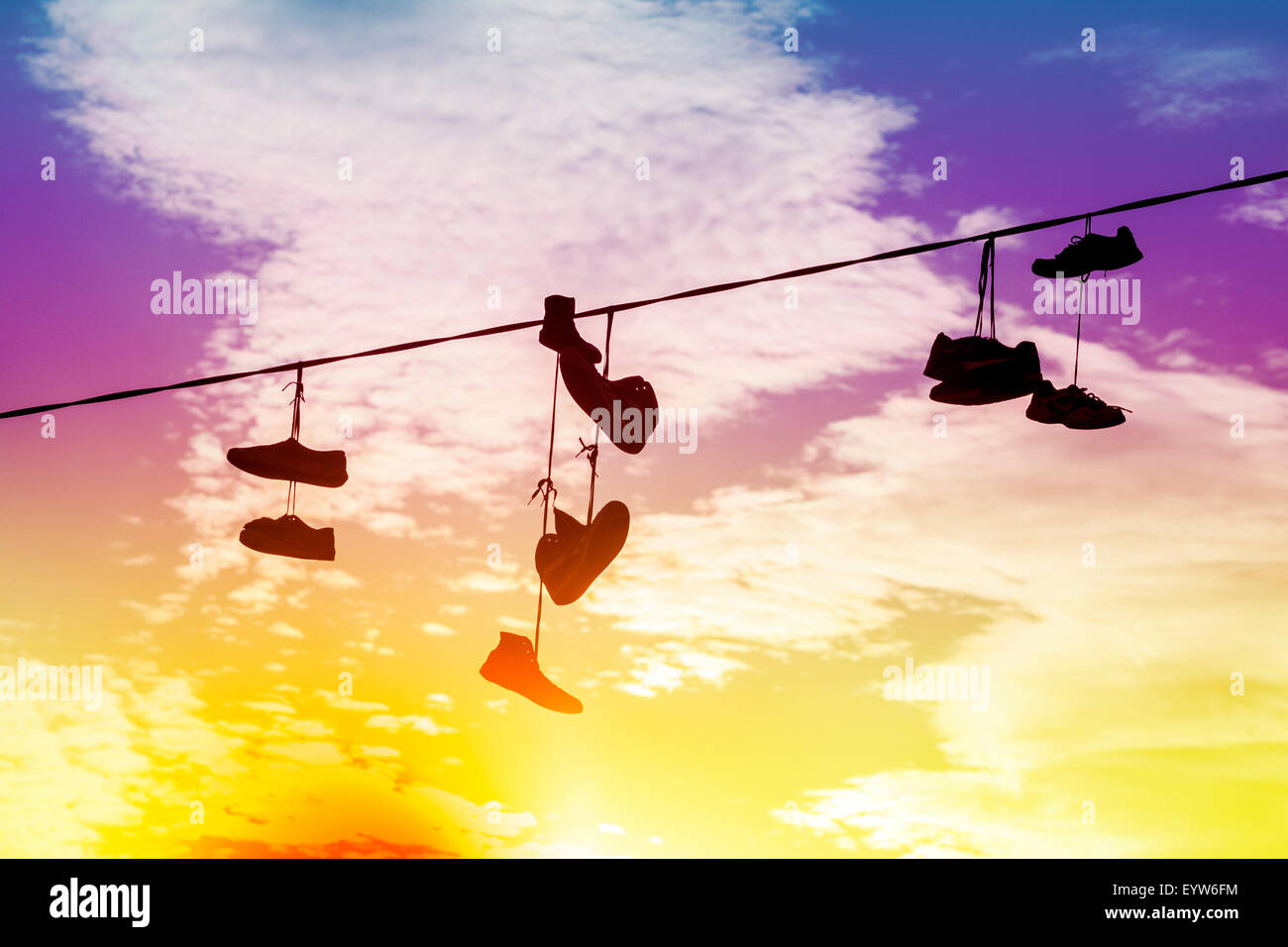 Silhouettes de tons Vintage shoes hanging sur le câble au coucher du soleil. Banque D'Images