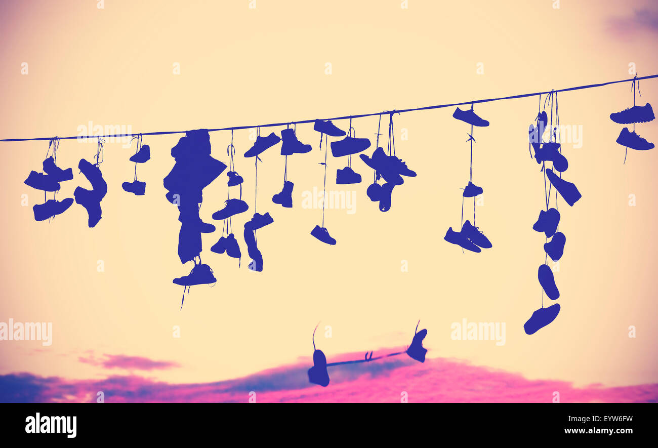 Silhouettes de tons Vintage shoes hanging sur le câble au coucher du soleil. Banque D'Images