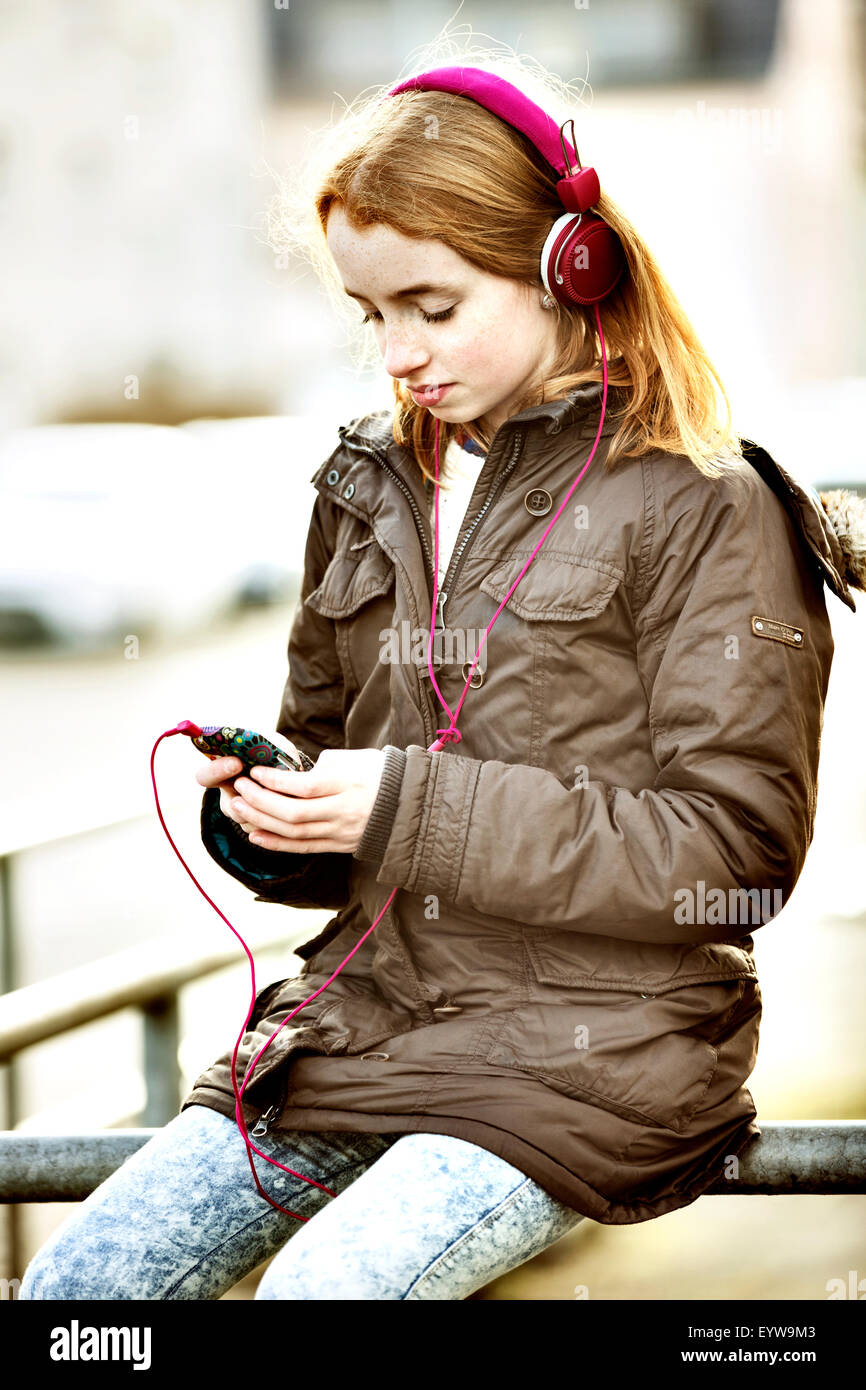 Fille, à tête rouge, avec le smartphone et un casque dans la ville Banque D'Images