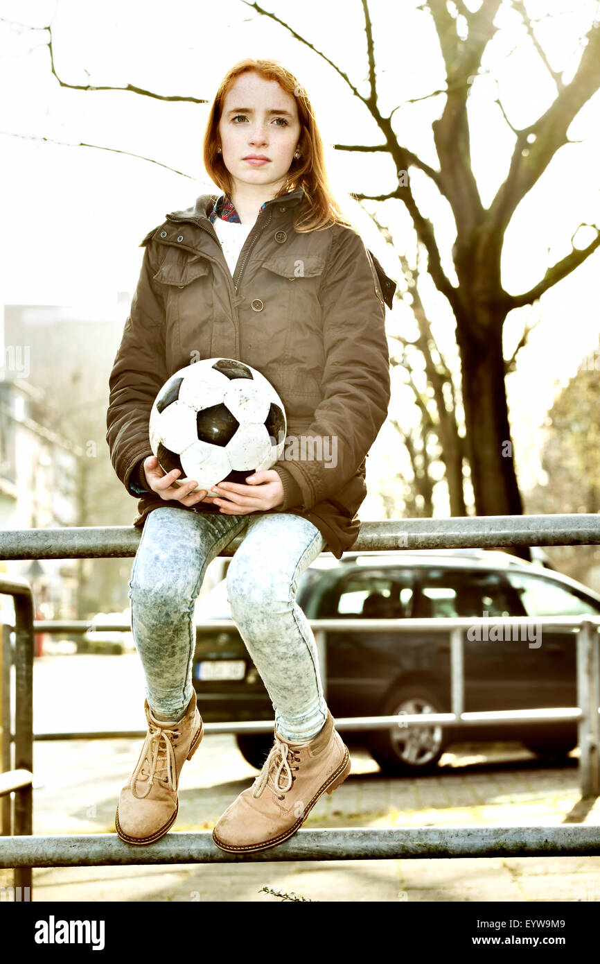Fille, à tête rouge, assise sur une balustrade avec un ballon de soccer, football, Cologne, Rhénanie du Nord-Westphalie, Allemagne Banque D'Images