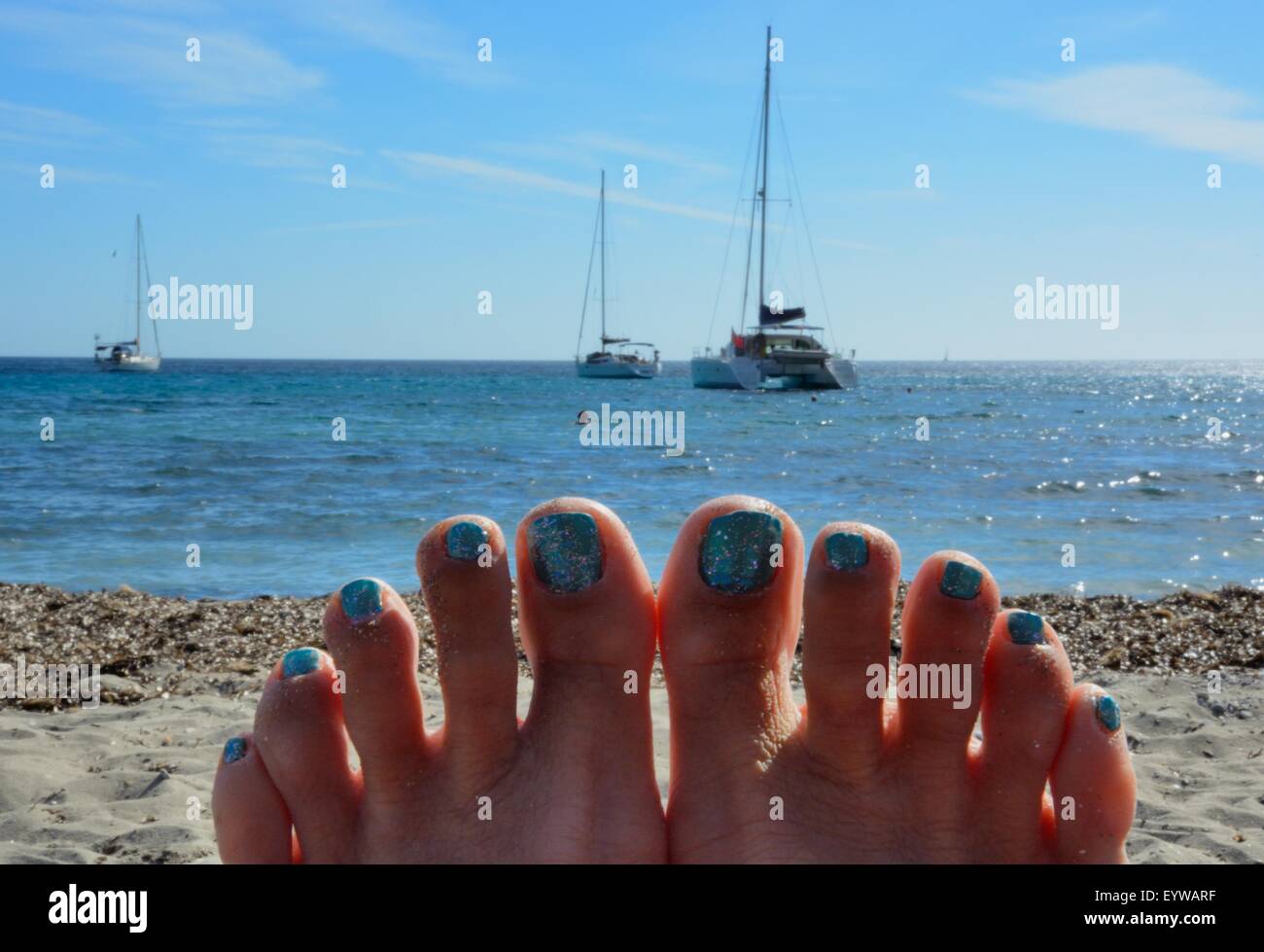 Des toenails peints pointent vers le ciel tout en se relaxant sur une plage en vacances. Banque D'Images