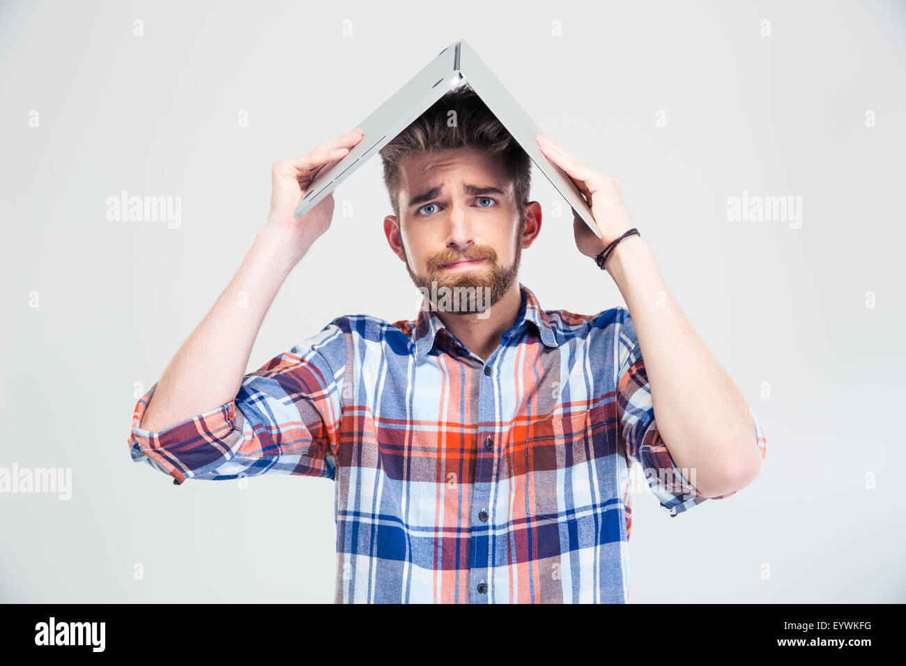 Casual man holding laptop sur sa tête comme toit de maison isolé sur un fond blanc. Looking at camera Banque D'Images
