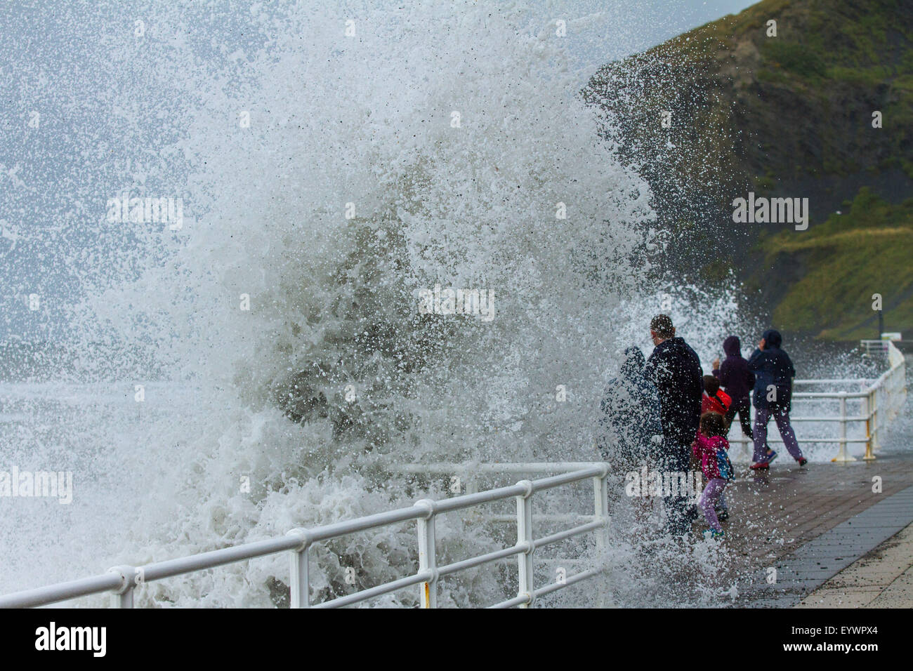 Aberystwyth, Pays de Galles, Royaume-Uni. 4 août 2015. Le temps orageux. Une houle de 5 à 8 pieds, vents forts et une marée haute à cmbine lash Aberystwyth front de mer avec des vagues énormes. Une famille en vacances à jouer en esquivant les vagues sur la promenade du front de mer Crédit : Alan Hale/Alamy Live News Banque D'Images