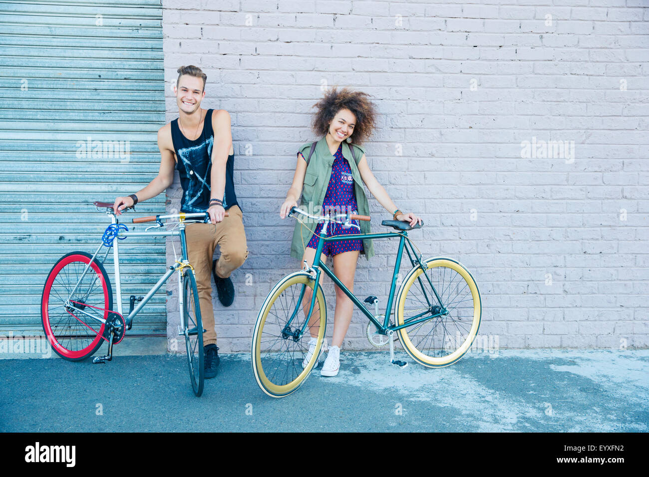 Portrait jeune homme et jeune femme avec des vélos à paroi urbaine Banque D'Images