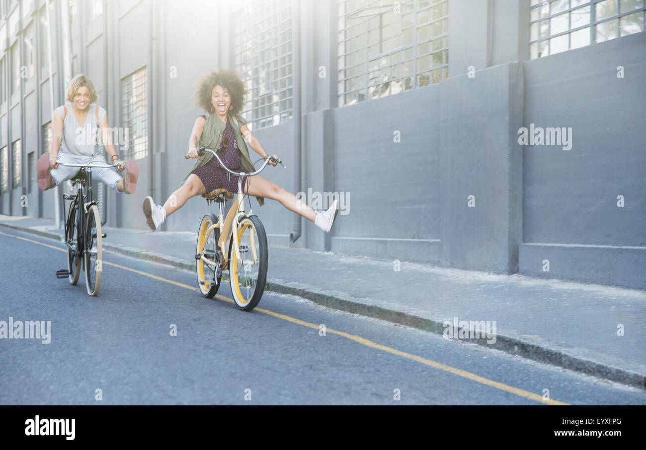 Les femmes espiègles sur les bicyclettes de cabotage vers le bas de la rue en milieu urbain Banque D'Images