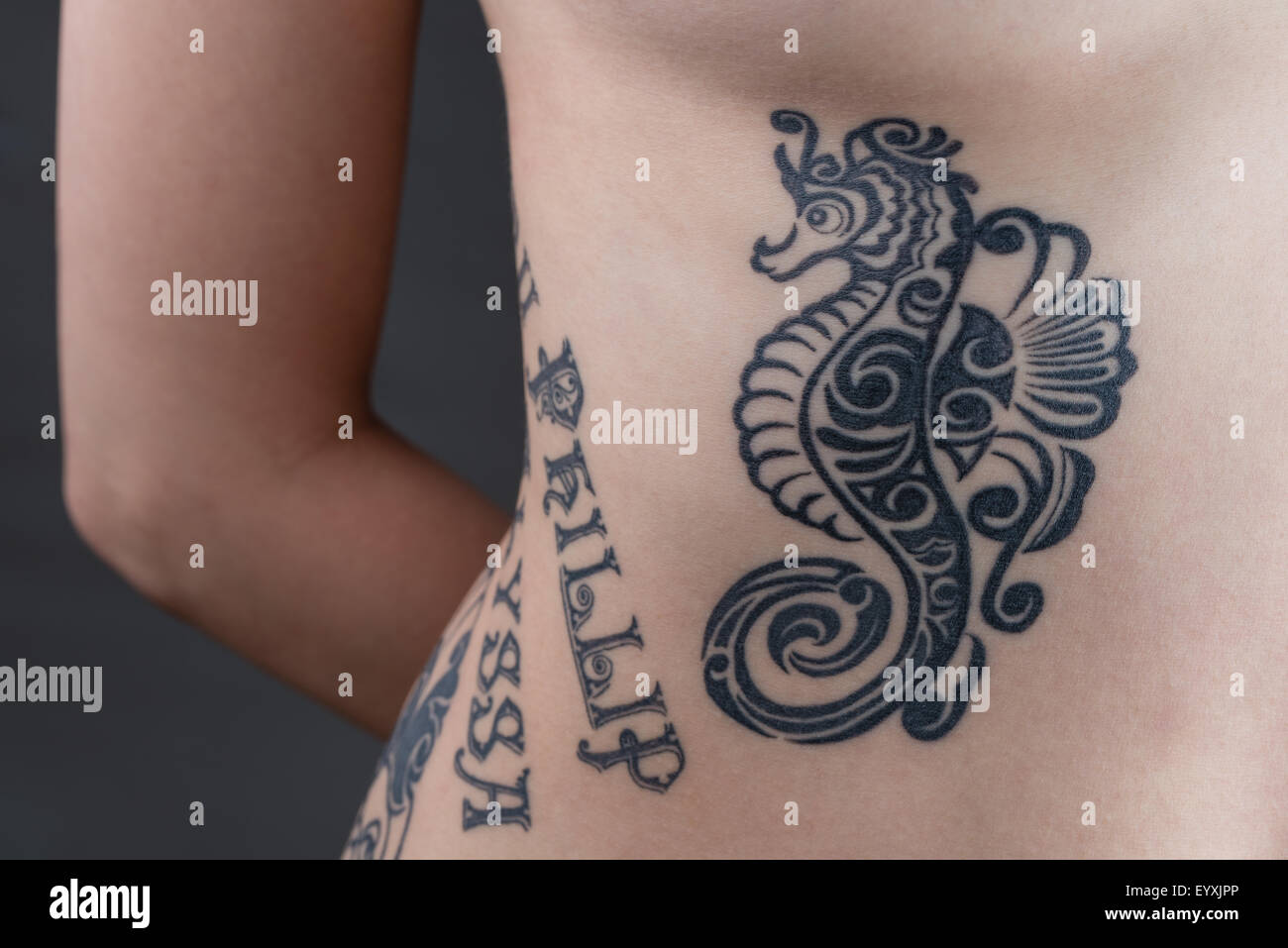 Un tatouage d'un hippocampe noir style tribal avec le nom des enfants s'enroulant autour d'une femme ses côtes. Banque D'Images