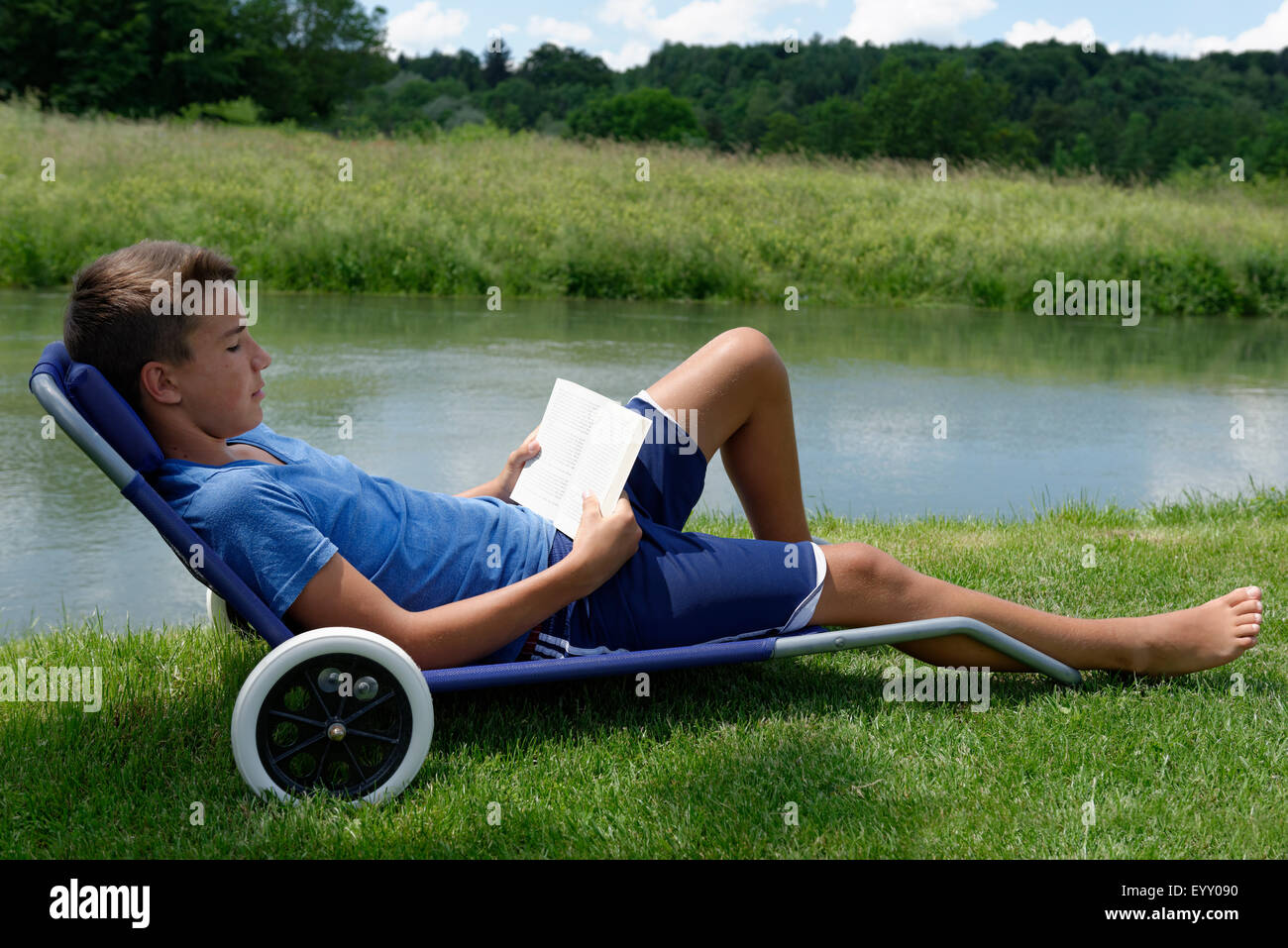Garçon couché dans un transat, lire un livre, à côté de la rivière, Loisach, Haute-Bavière, Bavière, Allemagne Banque D'Images