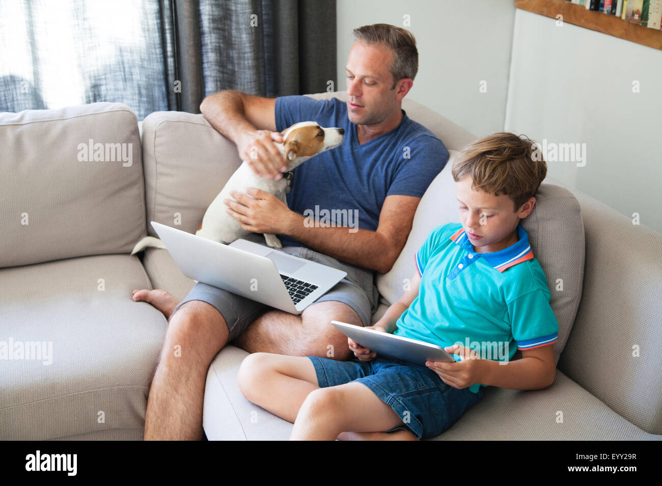 Portrait père et fils en utilisant la technologie sur canapé Banque D'Images