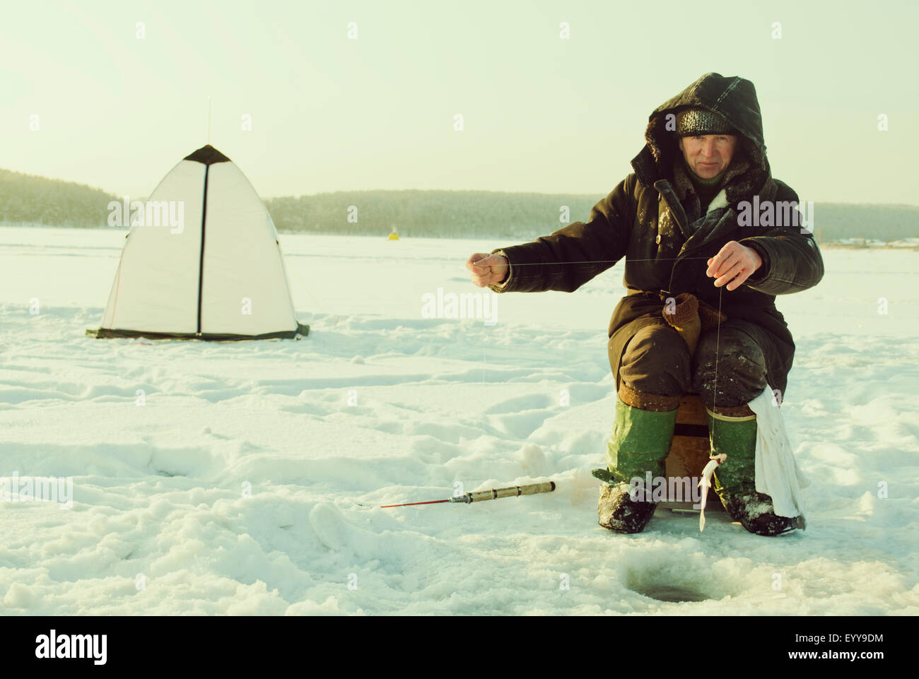 Caucasian man pêche sur glace sur le lac à distance Banque D'Images