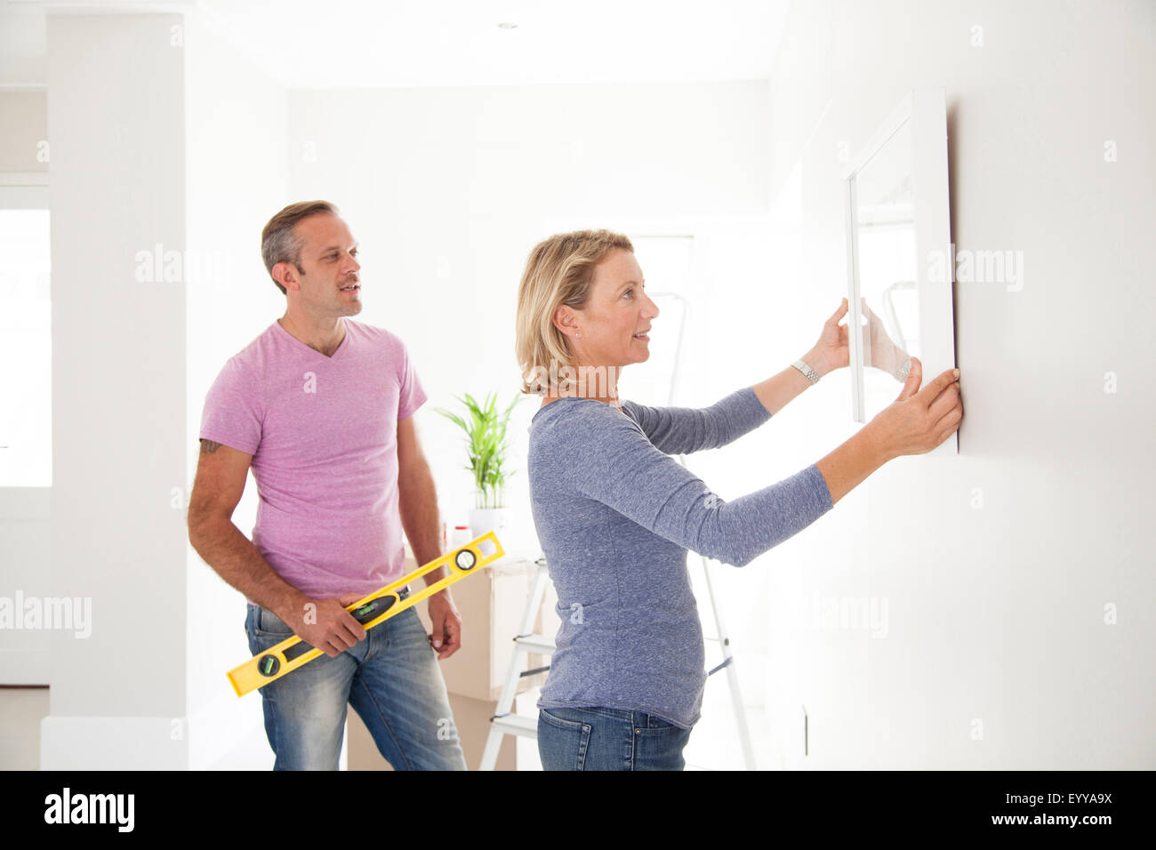 Caucasian couple hanging photo in new home Banque D'Images