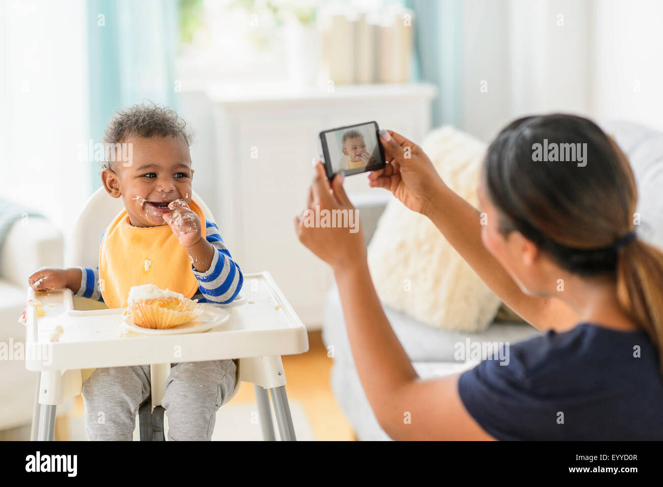 Mixed Race mother photographing messy baby boy in chaise haute Banque D'Images
