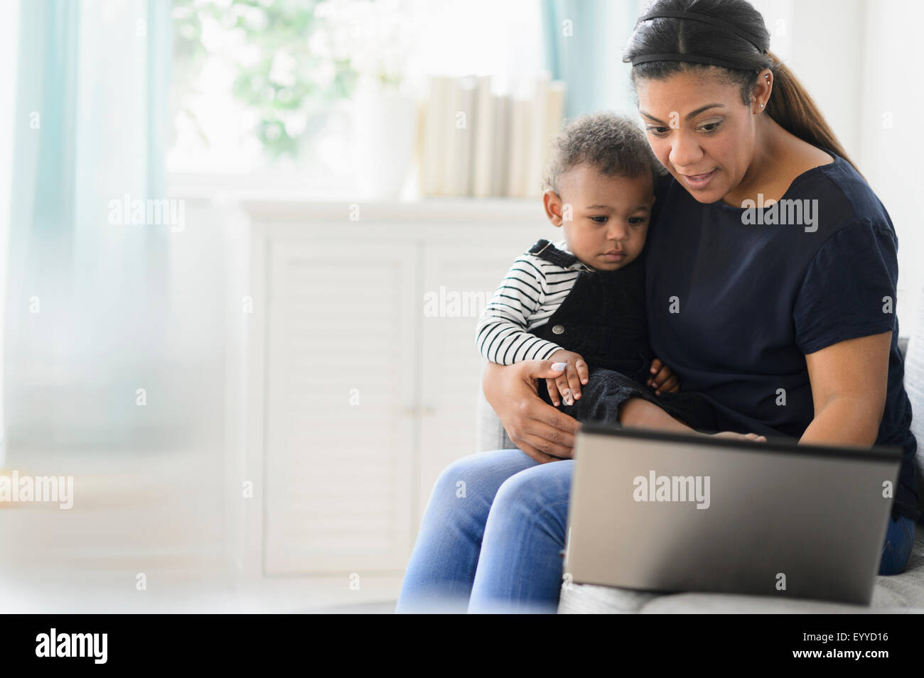 Mixed Race mère à l'aide d'un ordinateur portable avec son bébé dans la salle de séjour Banque D'Images