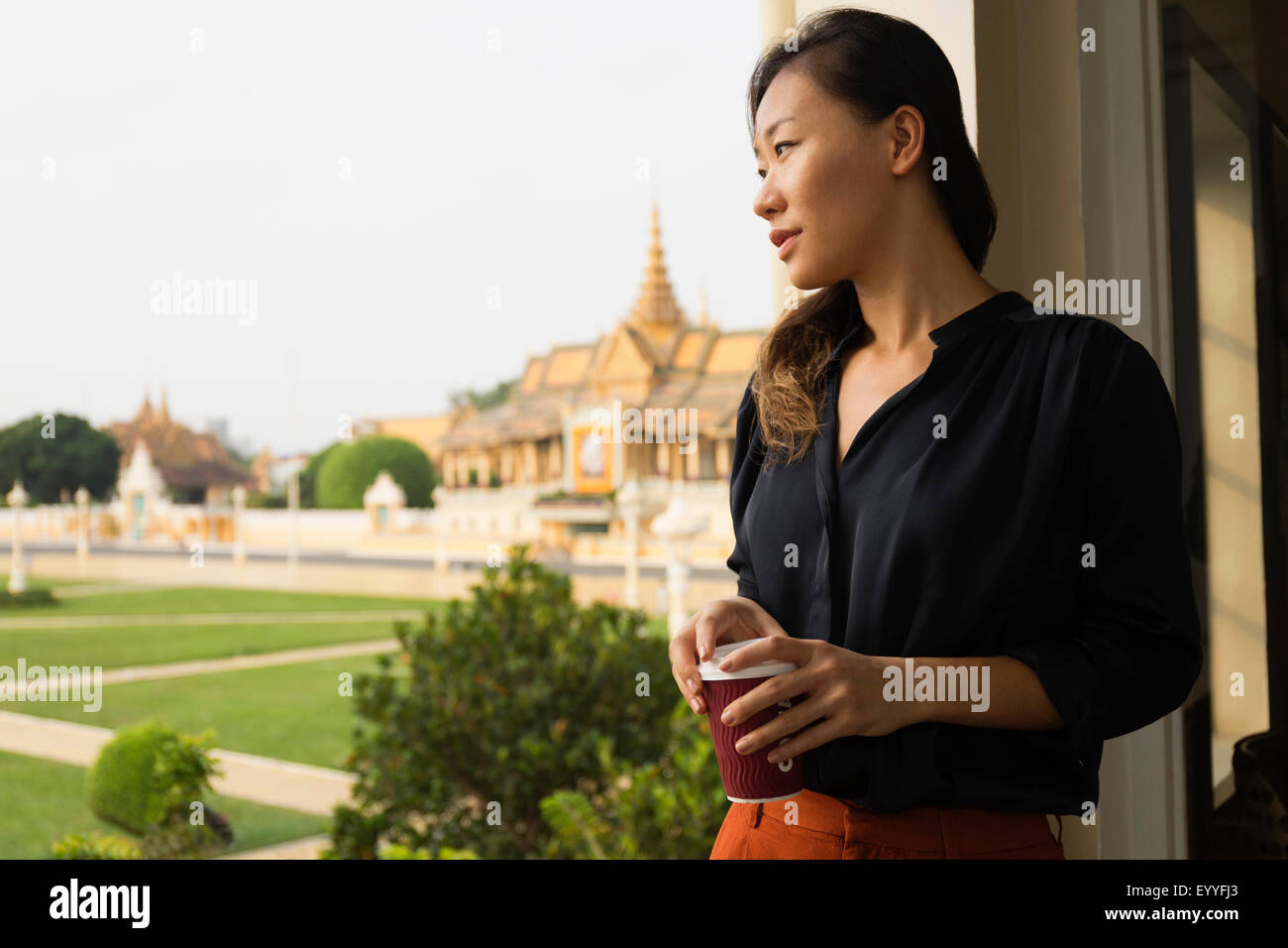 Asian businesswoman admiring view from cafe fenêtre, Phnom Penh, Cambodge Banque D'Images