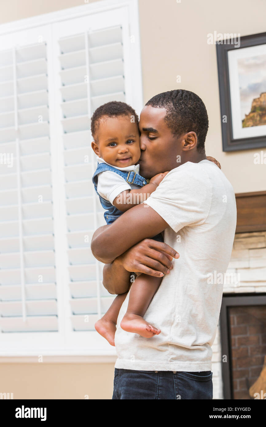Black father kissing baby son in living room Banque D'Images