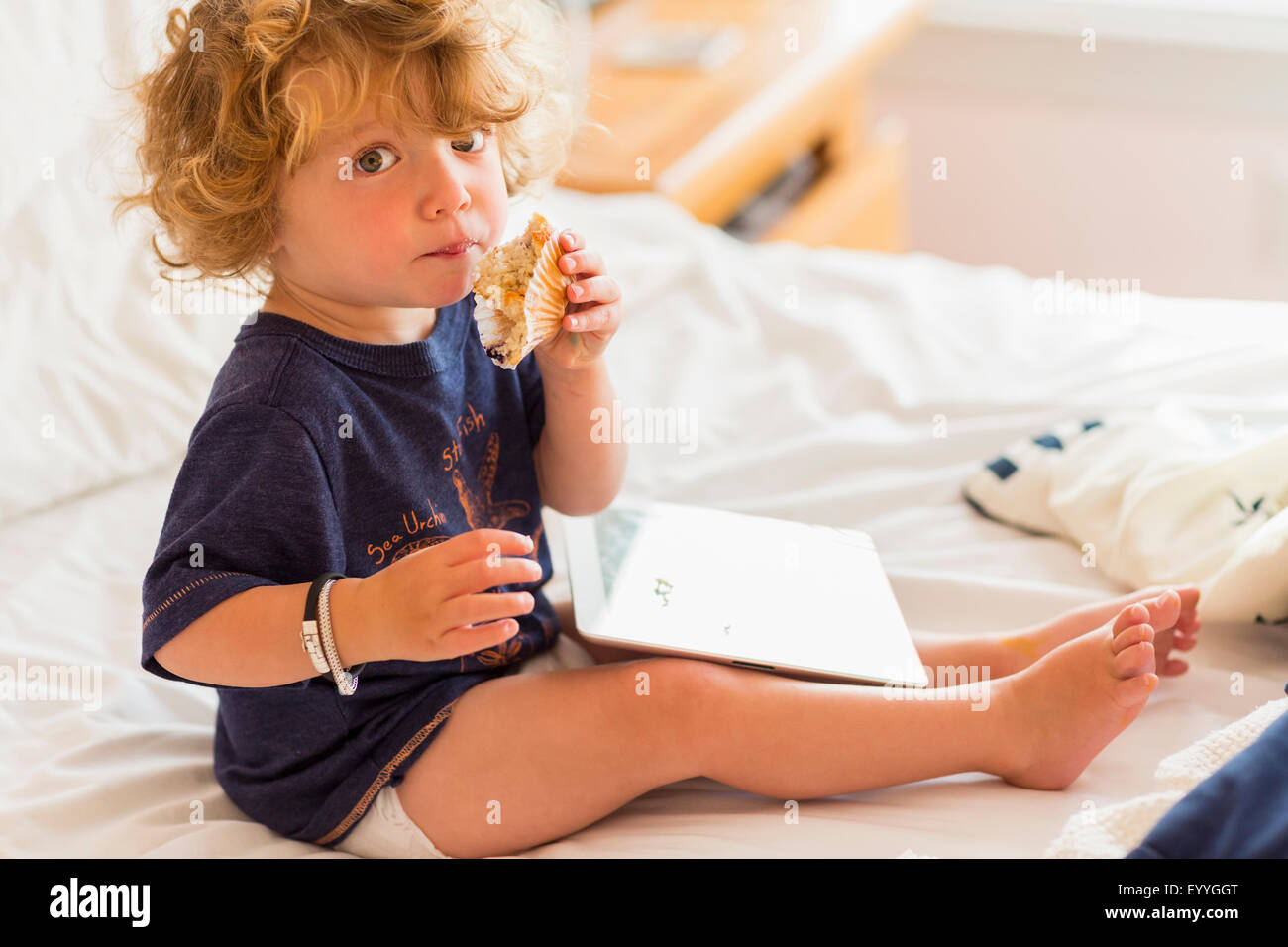 Caucasian baby boy eating et using digital tablet on bed Banque D'Images