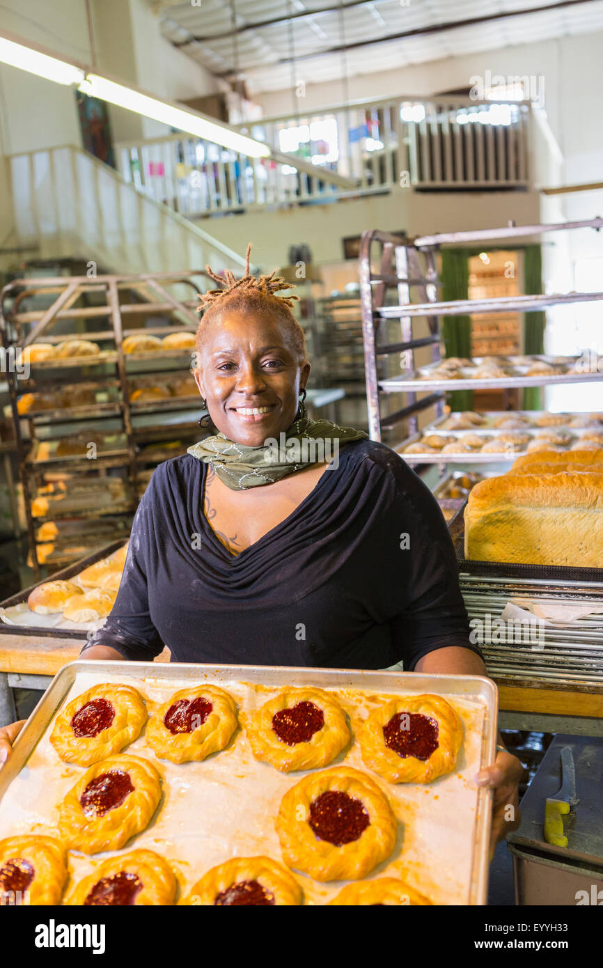 Baker holding tray noir de pâtisseries en cuisine boulangerie Banque D'Images