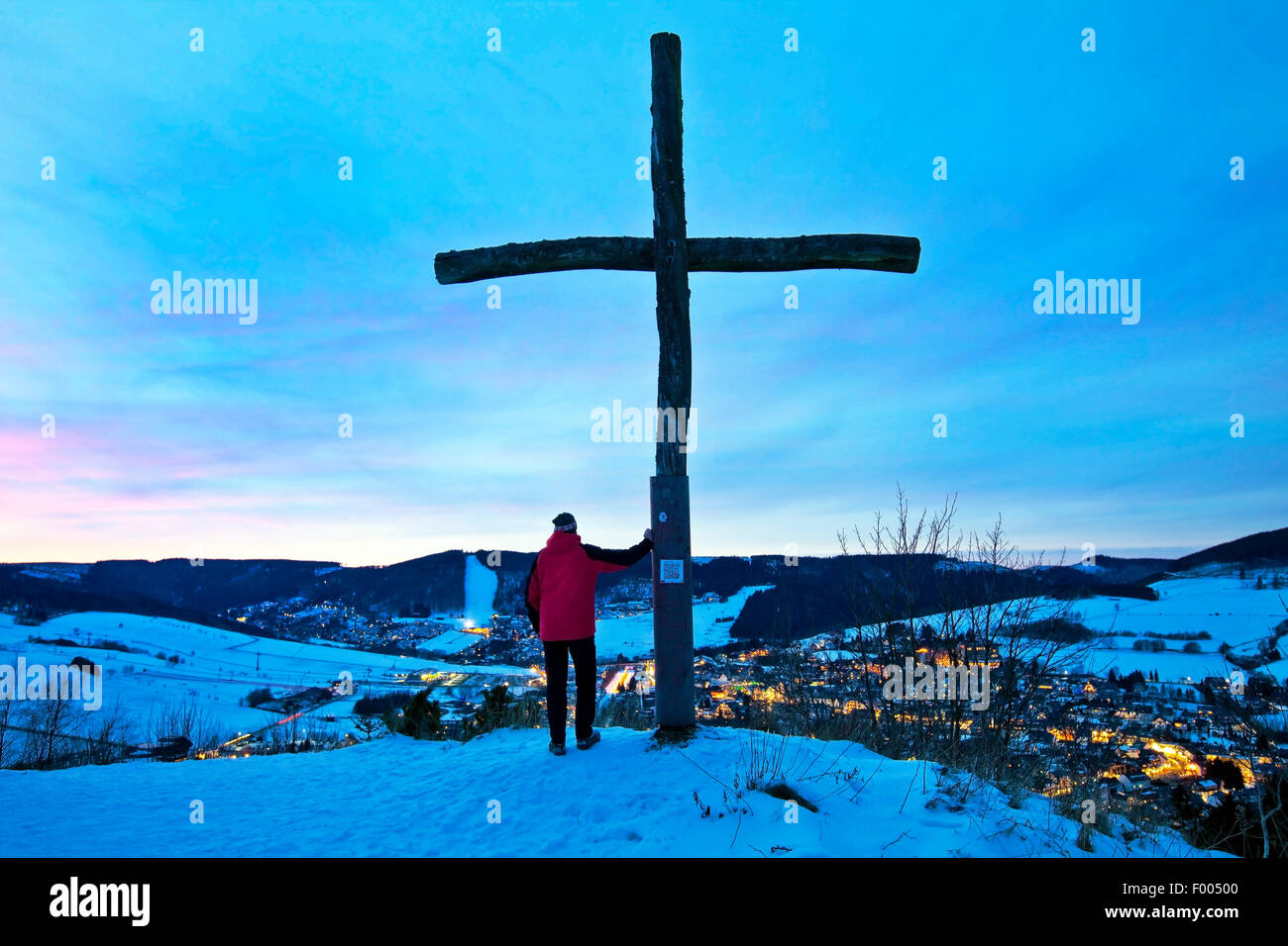 Homme à côté de croix sur Oerenberg sur la montagne de profiter de la vue de paysage hivernal dans la soirée, l'Allemagne, Hesse, Sauerland, Willingen Banque D'Images