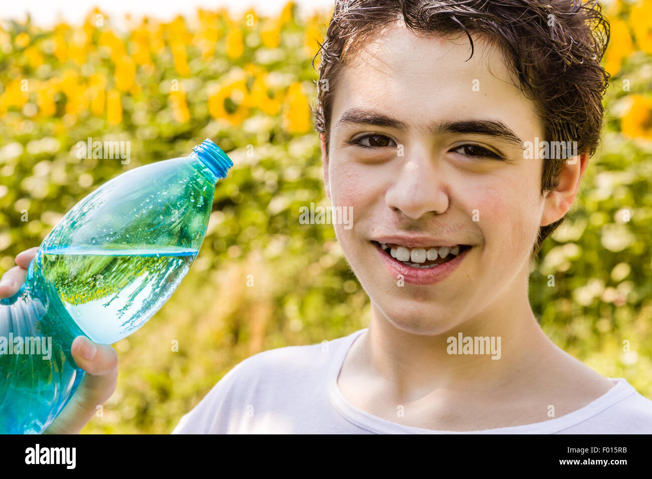 Salon de l'environnement - Caucasian boy dans un champ de tournesols est sur le point de boire de l'eau claire d'une bouteille en plastique bleu vert d'étancher sa soif par une chaude journée d'été et lumineux Banque D'Images