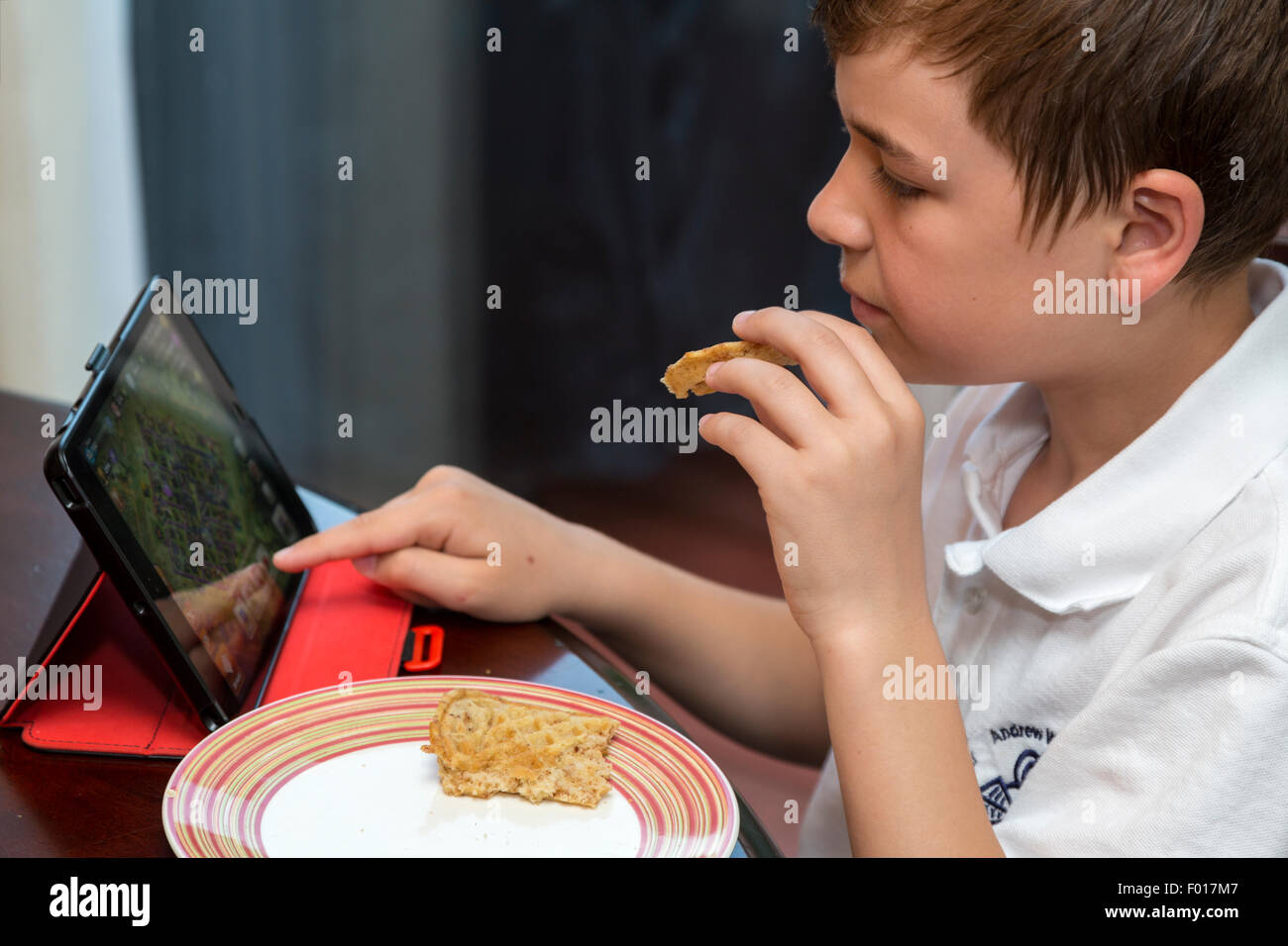 Jeune garçon à l'aide de l'iPad tout en mangeant le petit déjeuner. M. Banque D'Images
