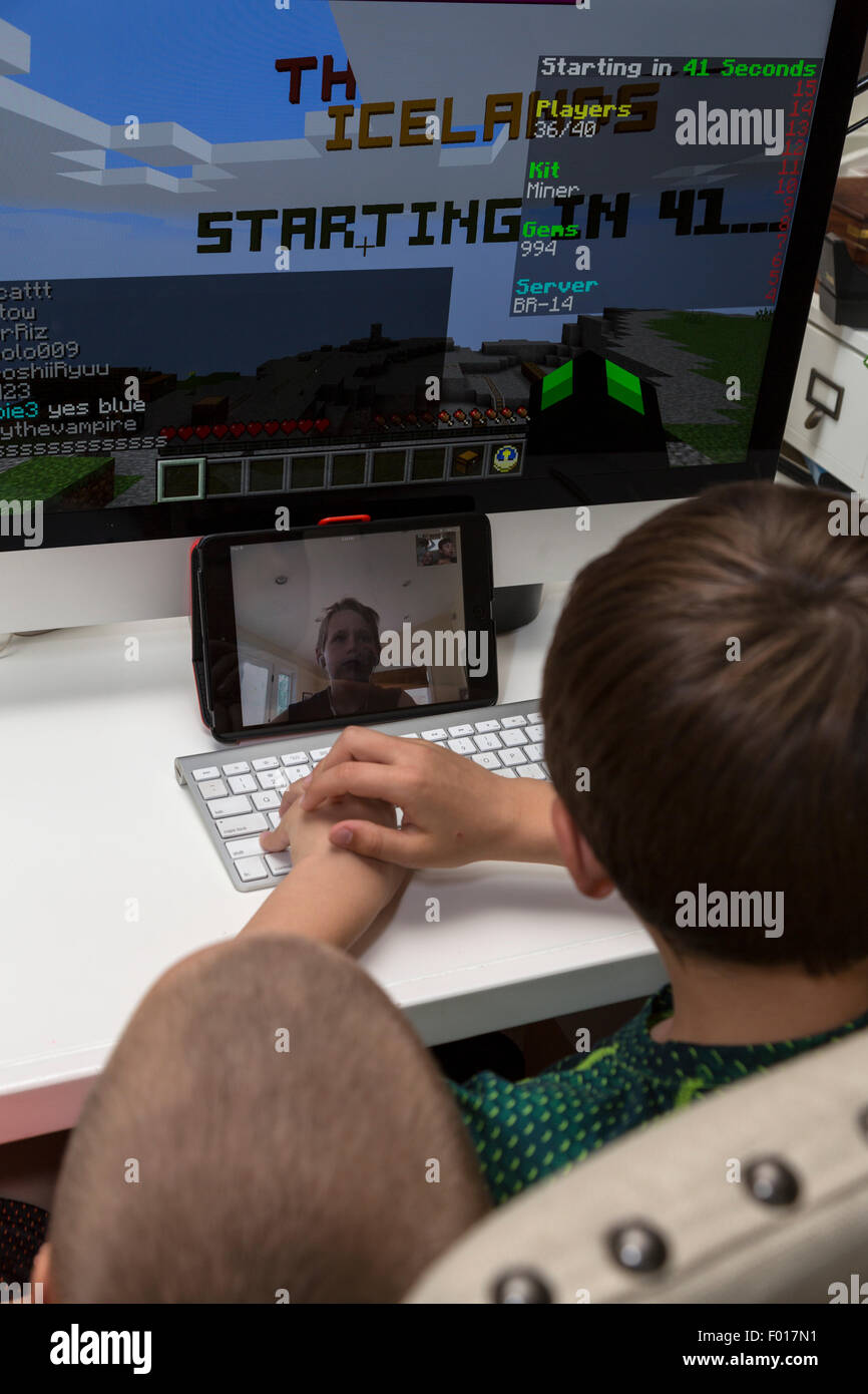 Deux garçons à jouer à des jeux vidéo avec un ami à l'aide de Facetime pour les communications longue distance. M. Banque D'Images