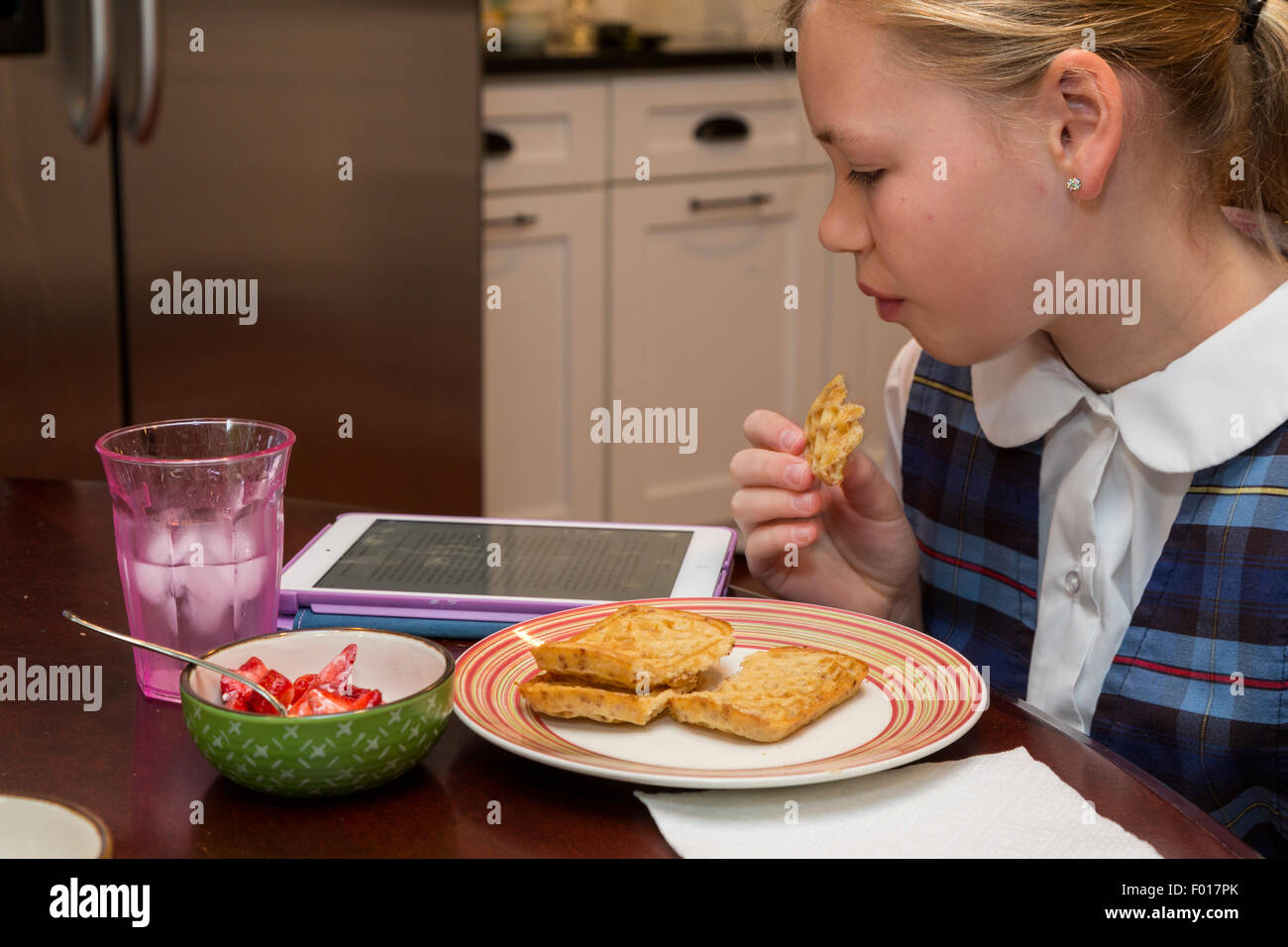 Jeune fille (11 ans) La lecture sur son iPad en mangeant le petit déjeuner. M. Banque D'Images