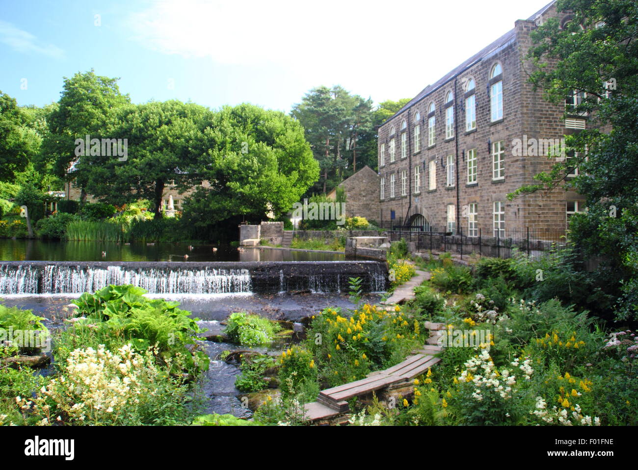 Les gens marcher sur la passerelle publique en bois par Bamford Mill et Weir dans le Derbyshire Peak District England UK - été Banque D'Images