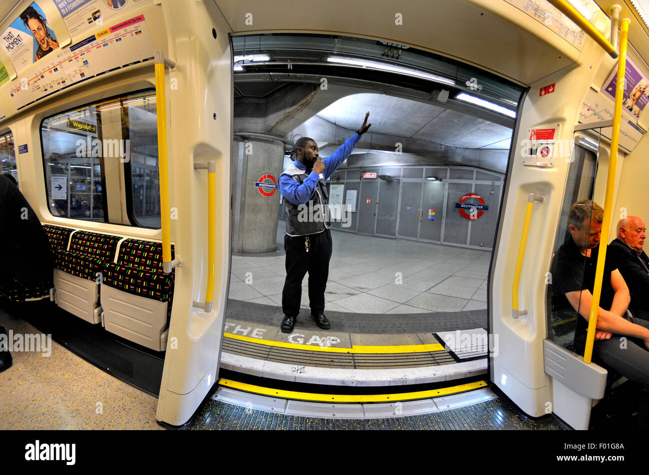 Londres, Angleterre, Royaume-Uni. London Underground tube train sur la plate-forme à Westminster Station. La signalisation de l'employé tout clair Banque D'Images