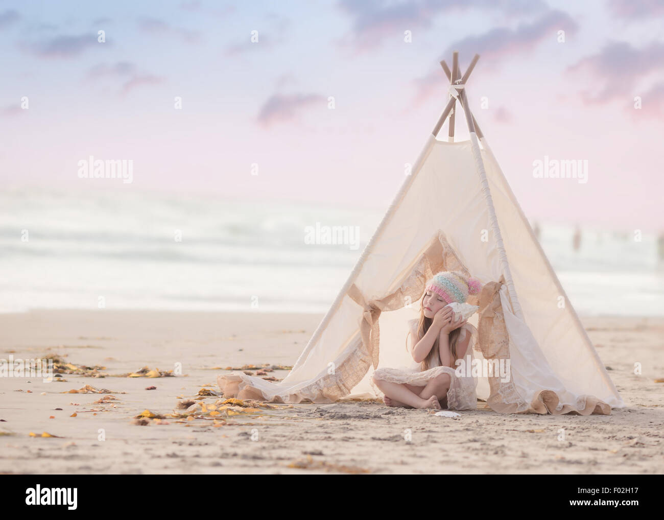Fille assise dans une wigwam sur la plage à l'écoute d'un bord de mer, Californie, Etats-Unis Banque D'Images