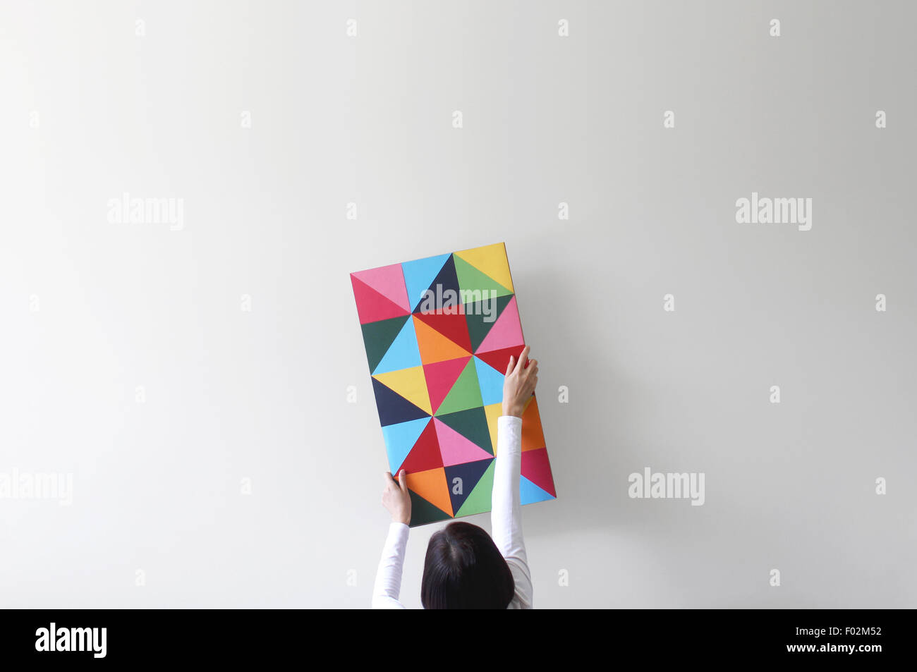 Femme décorant un mur blanc vide avec des œuvres d'art colorées Banque D'Images