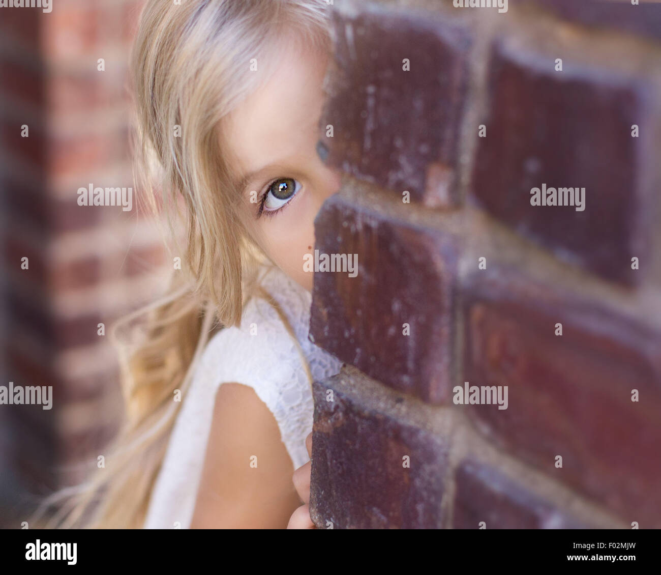 Girl peeking autour d'un mur de briques Banque D'Images
