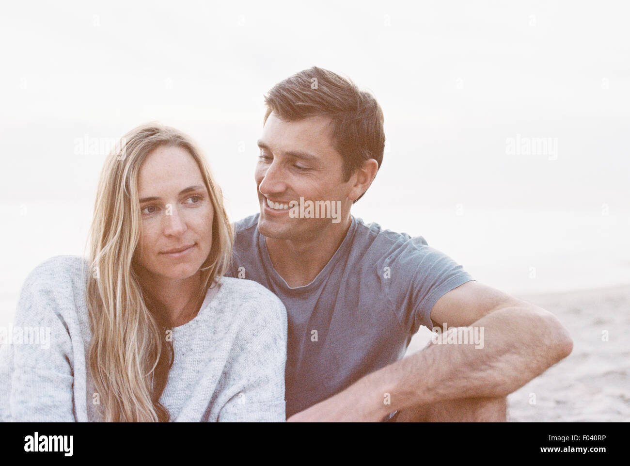 Un couple assis sur une plage, un homme et une femme avec leurs bras autour de l'autre et chefs ensemble. Banque D'Images