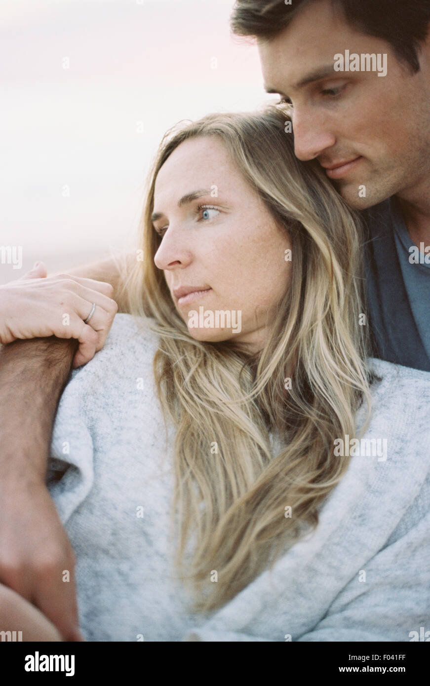Un couple, un homme et une femme assis sur une plage bras autour de l'autre, au crépuscule. Banque D'Images