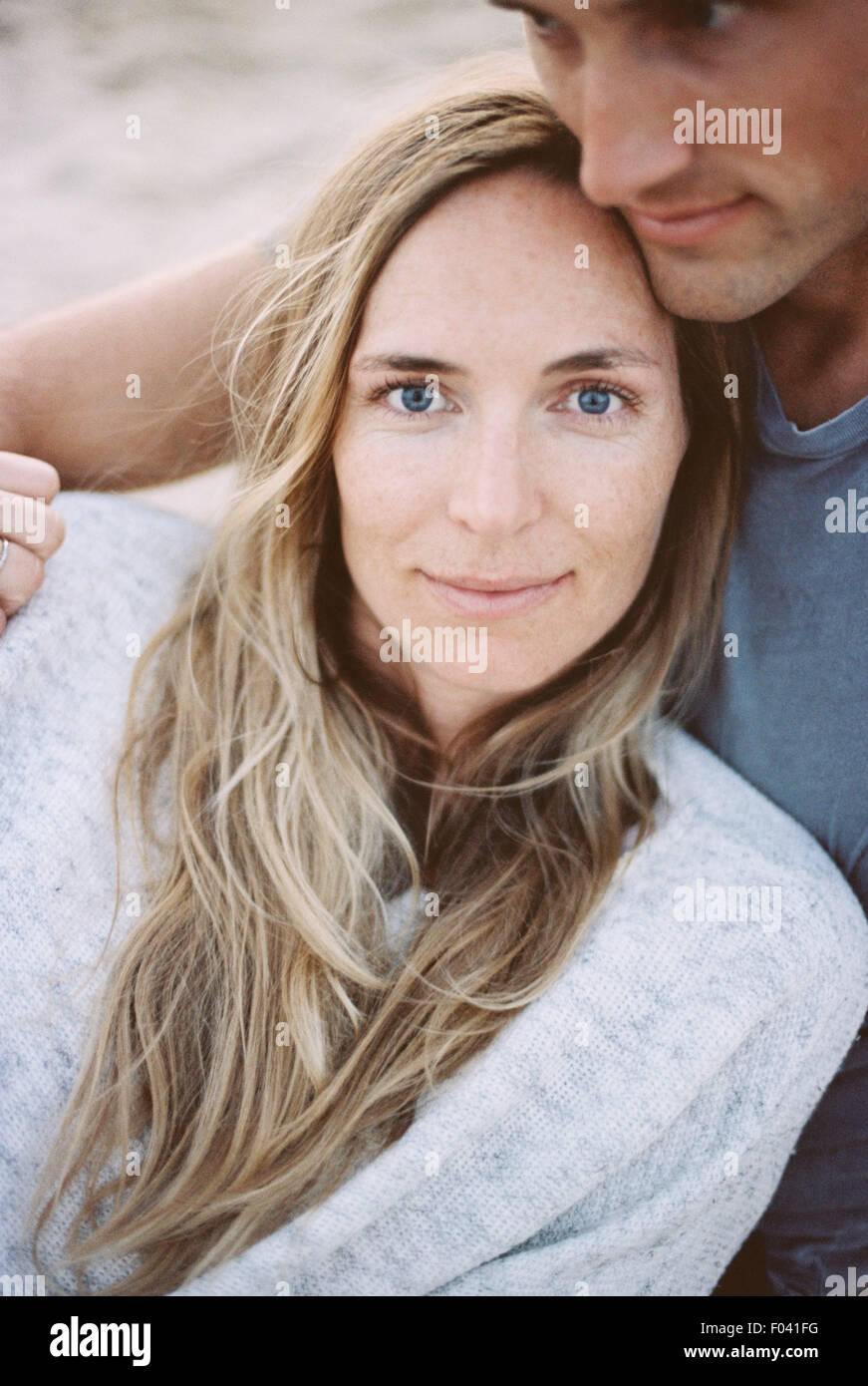 Un couple, un homme et une femme assis sur une plage bras autour de l'autre, au crépuscule. Banque D'Images